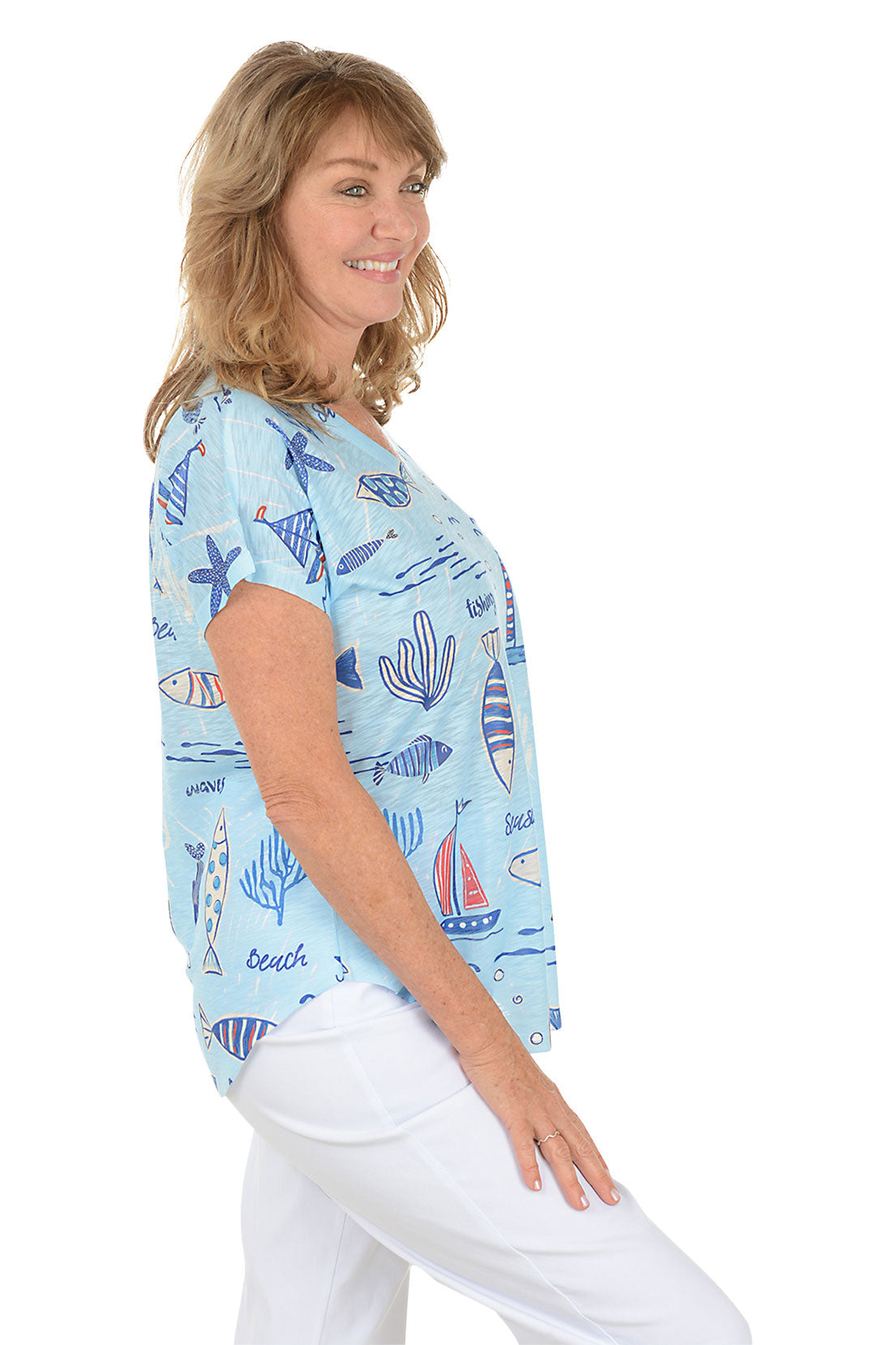 A woman wearing a blue short sleeve v-neck shirt with a fish and sailboat design. Side shot.