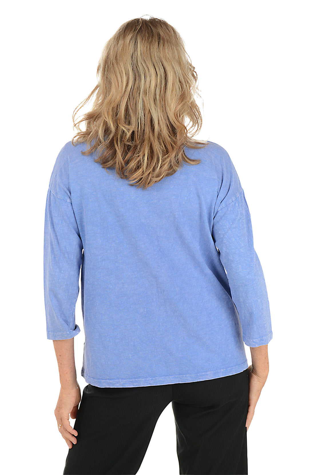 A woman wearing a 3/4 sleeve blue top with a palm tree pattern detail. Back shot.