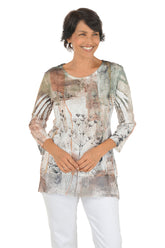 A front shot of a model wearing a patterned blouse with white pants on a white background