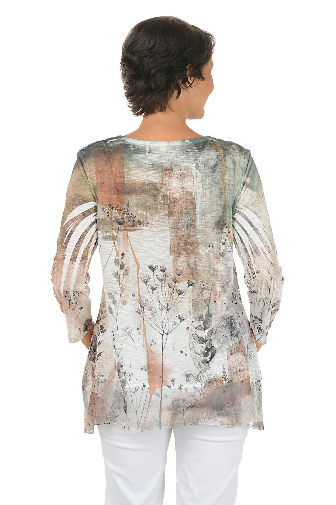 A back shot of a model wearing a patterned blouse with white pants on a white background