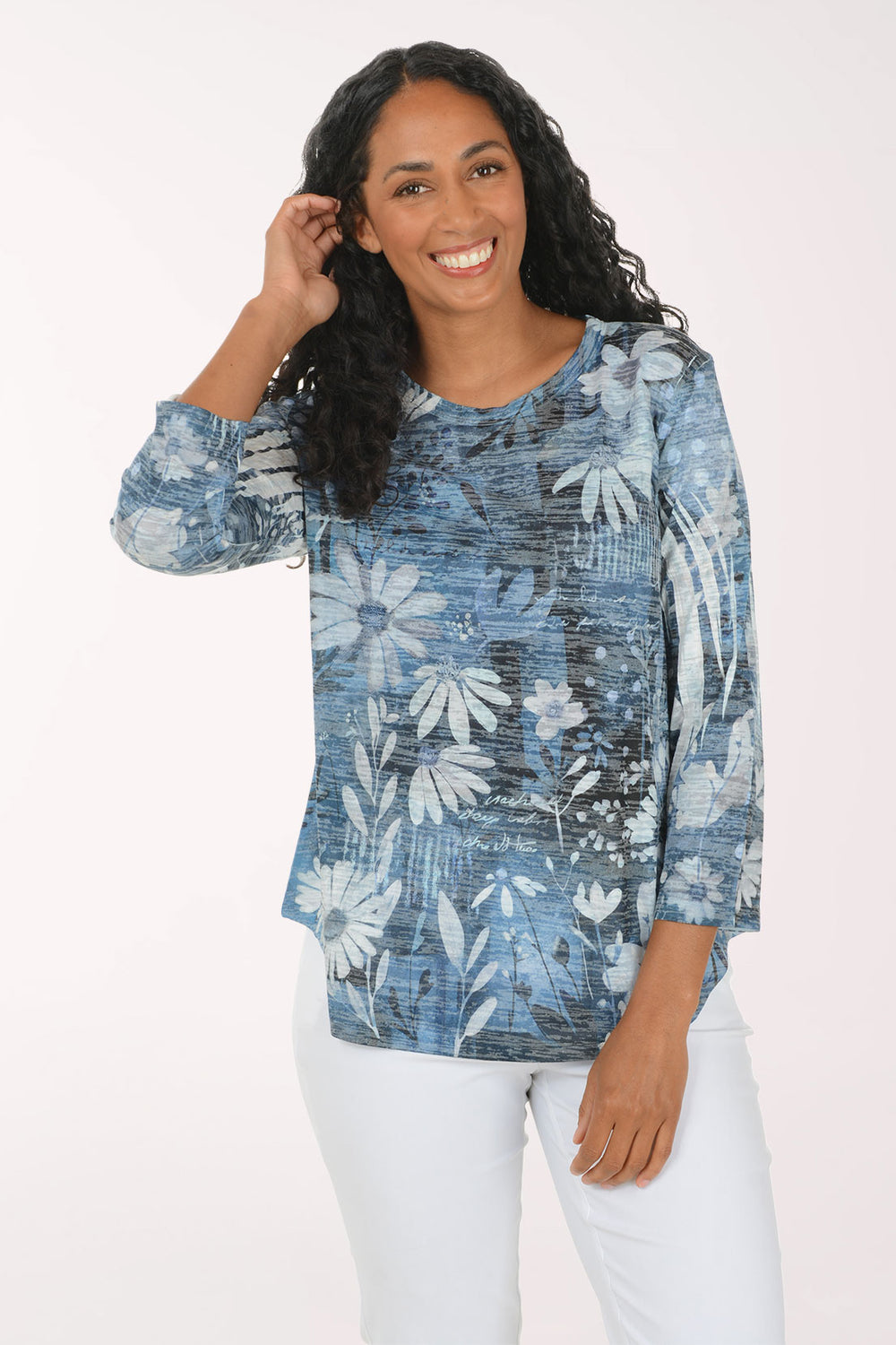 A woman modeling a blue and white floral print long-sleeve top with white pants, standing against a plain white studio background.