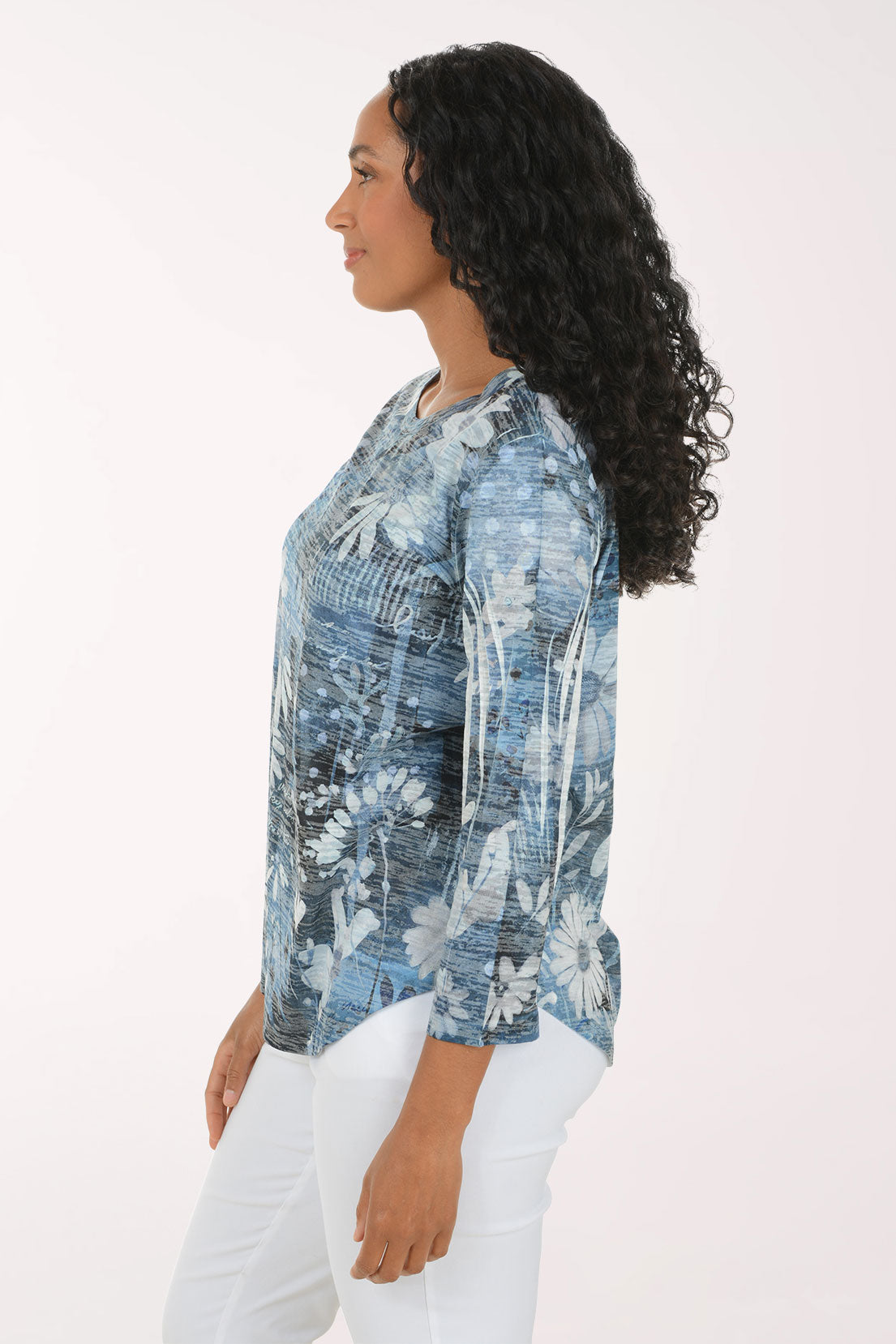 A woman modeling a blue and white floral print long-sleeve top with white pants, standing against a plain white studio background.