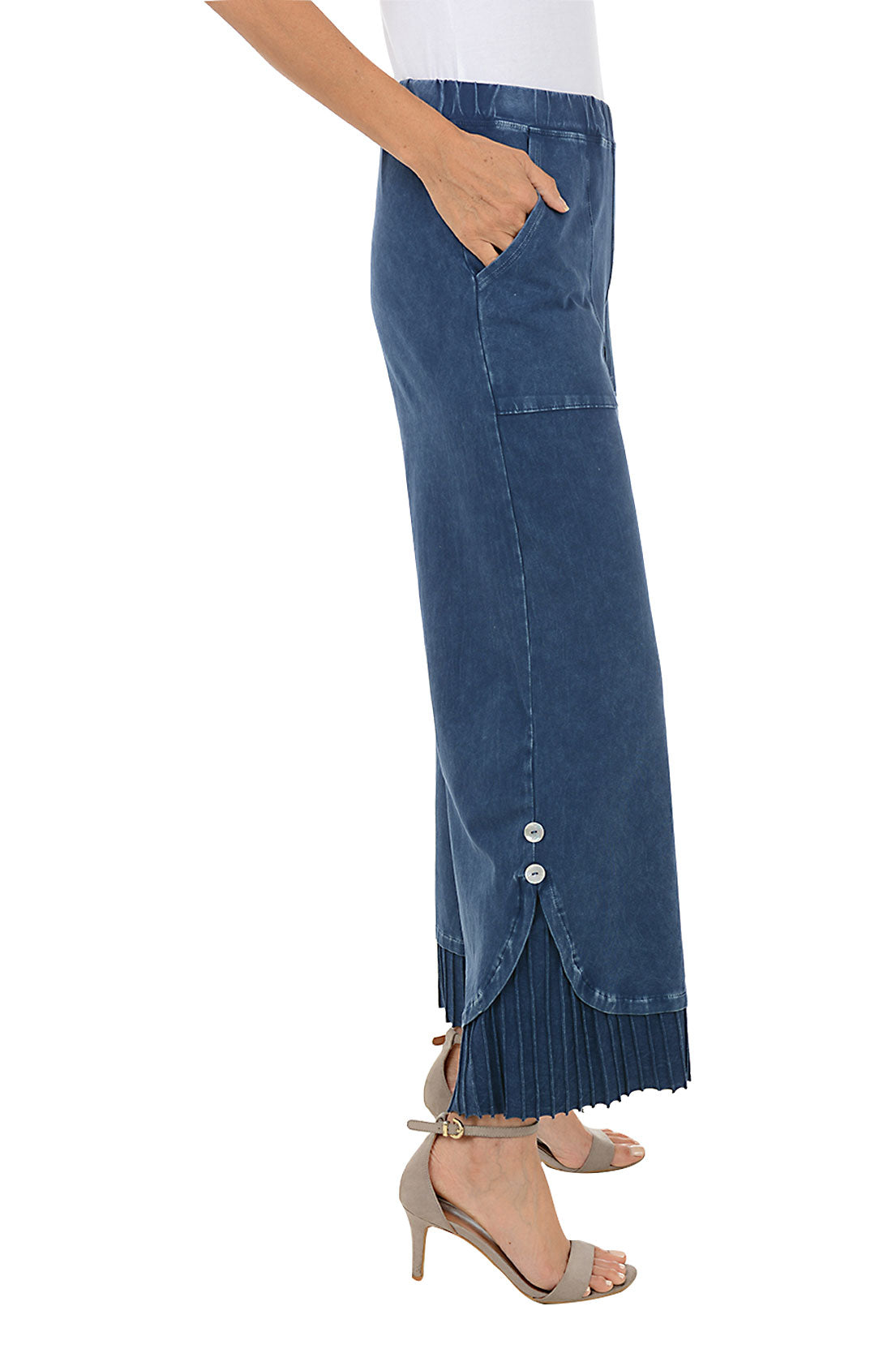 A side shot of a model wearing a pair of wide-leg, pleated hem pants with a mineral wash design. The pants have a high waist with a 1 1/2 inch elasticized waistband, dual front patch pockets, and a double button embellishment at the pleated hemline.