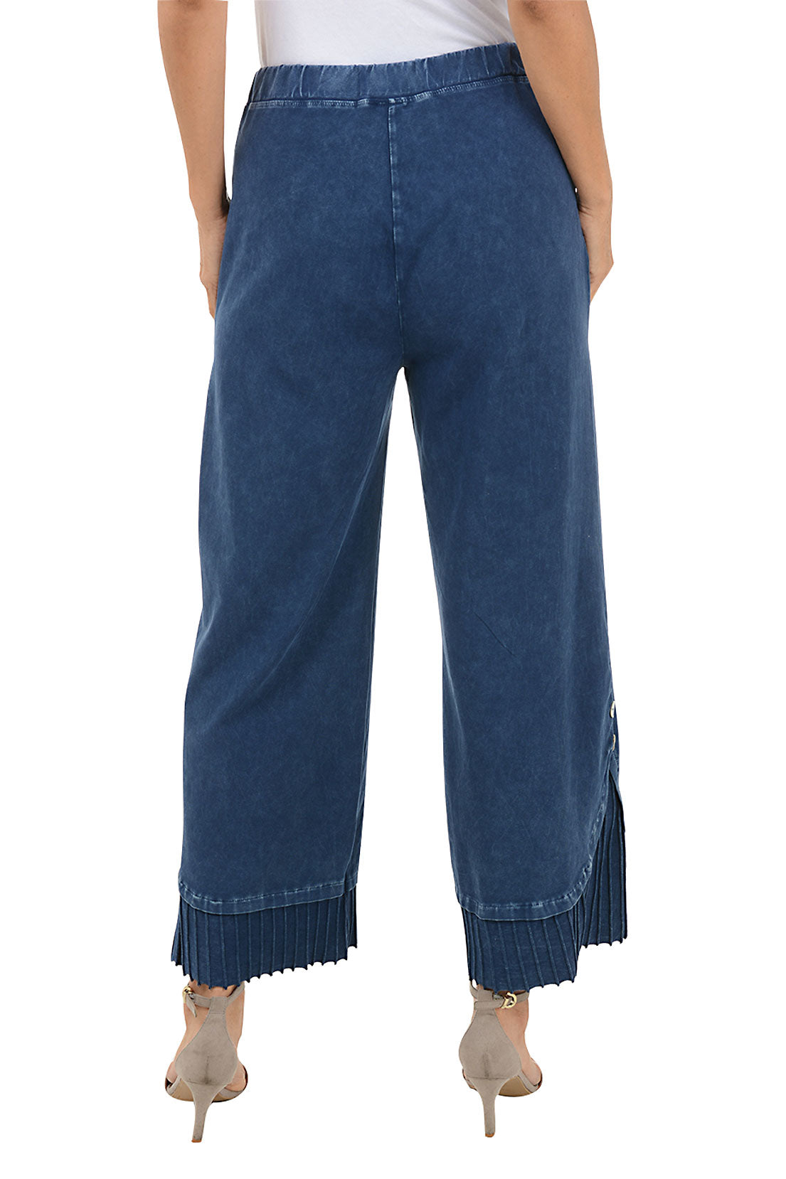 A back shot of a model wearing a pair of wide-leg, pleated hem pants with a mineral wash design. The pants have a high waist with a 1 1/2 inch elasticized waistband, dual front patch pockets, and a double button embellishment at the pleated hemline.