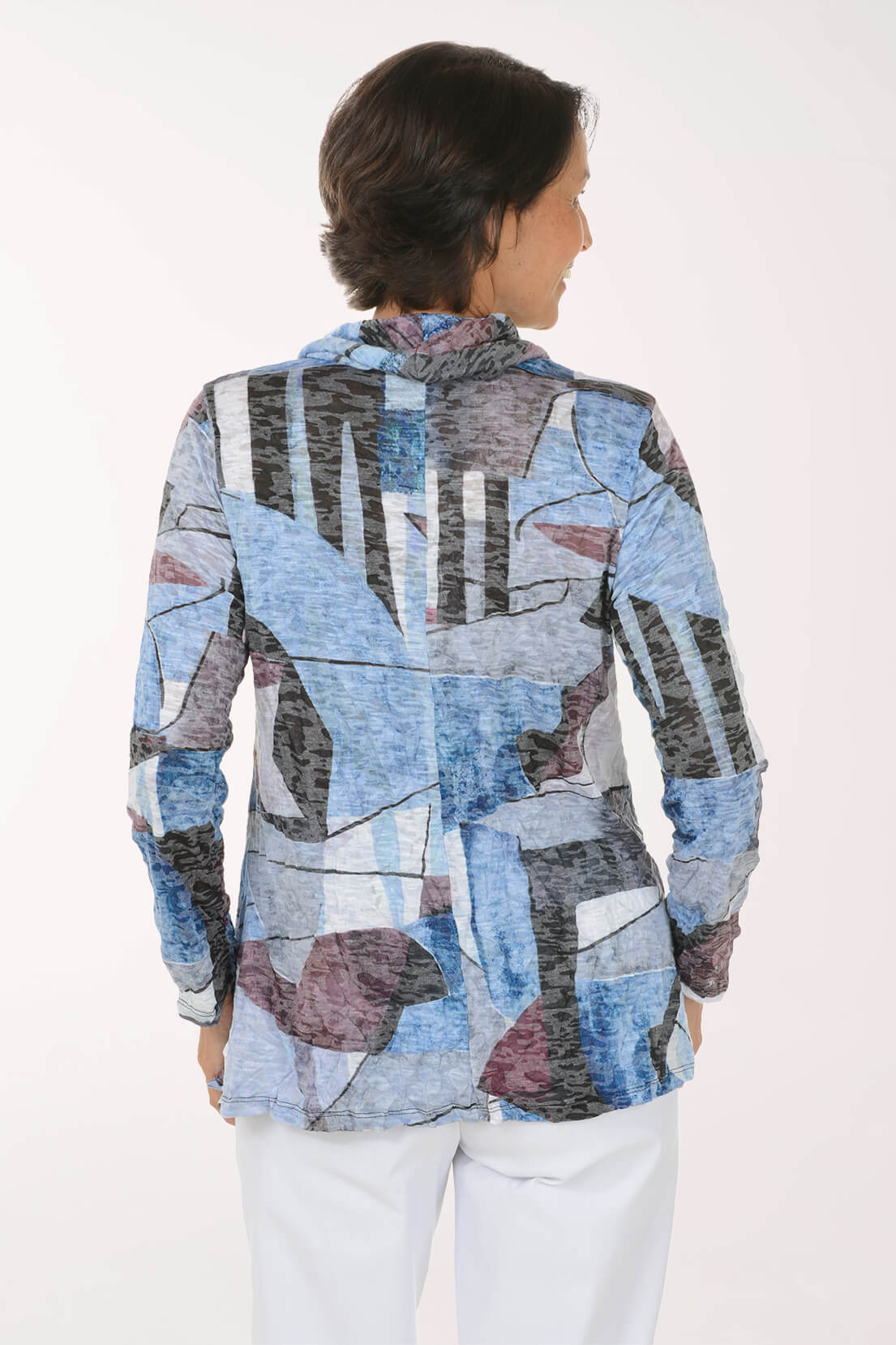 A woman shown from the back wearing a long-sleeve abstract print top with blue, gray, black, and mauve tones, paired with white pants, against a plain white background.