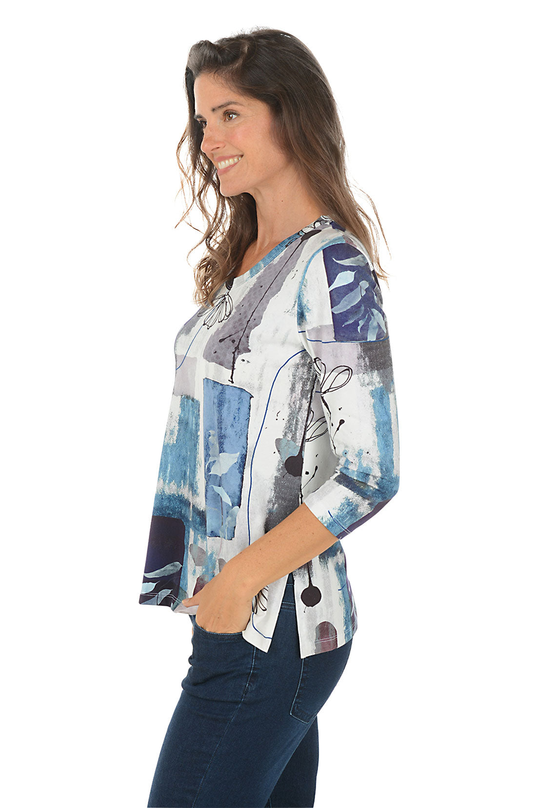 Woman wearing a colorful patterned top with blue jeans on a white background. Side shot.