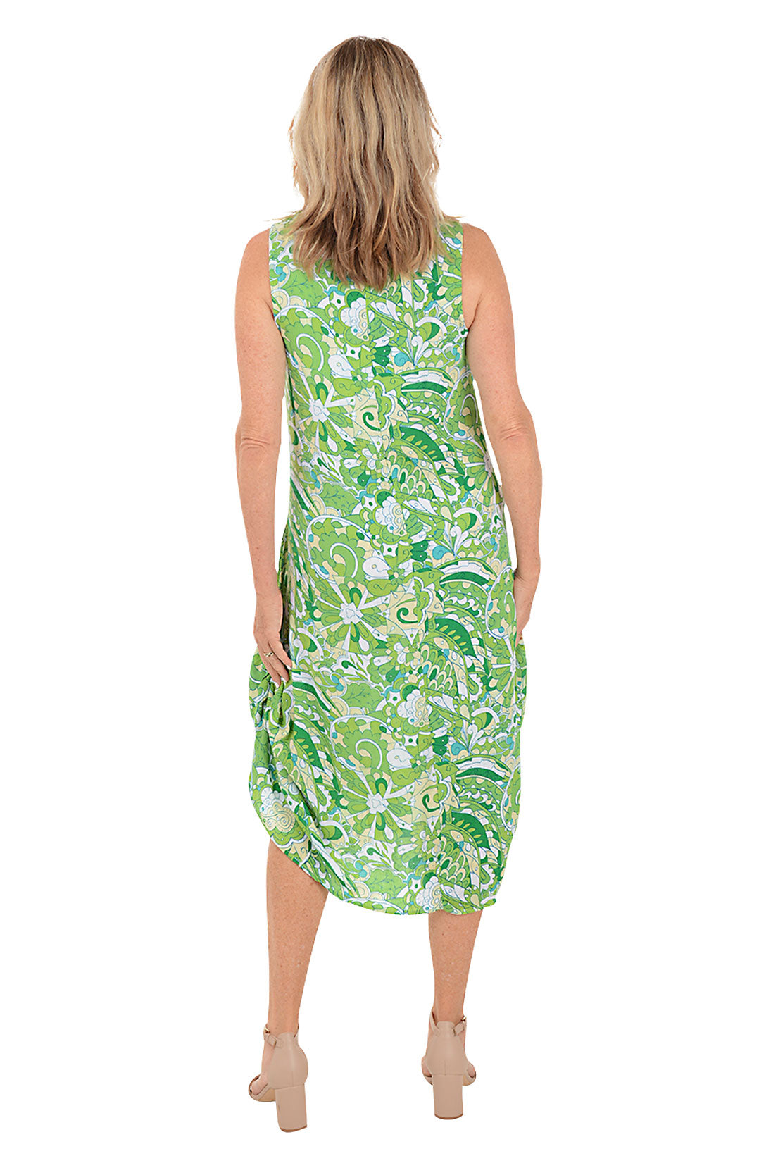 A back shot of a model wearing a sleeveless, knee-length, green and white paisley print dress with a scoop neckline, dual front patch pockets, and a shark bite hemline.