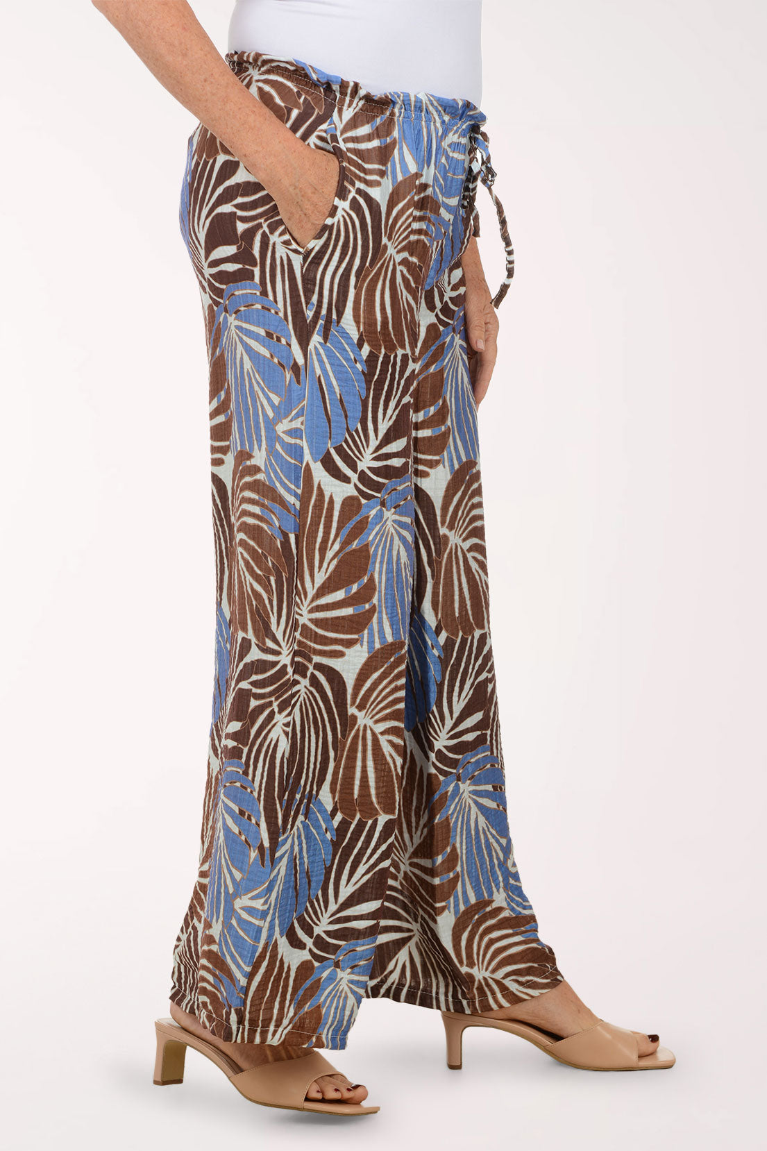 Tropical leaf patterned pants worn by a person on a white background