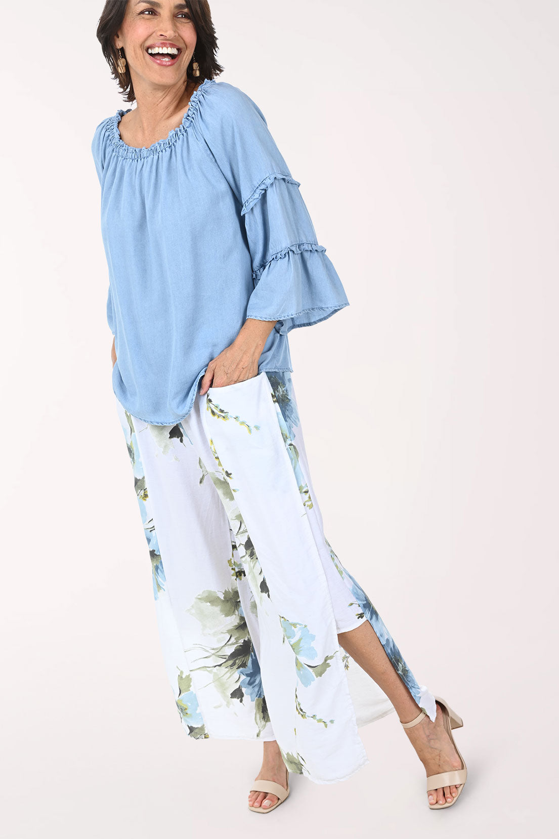 Woman wearing a light blue blouse and floral pants on a white background