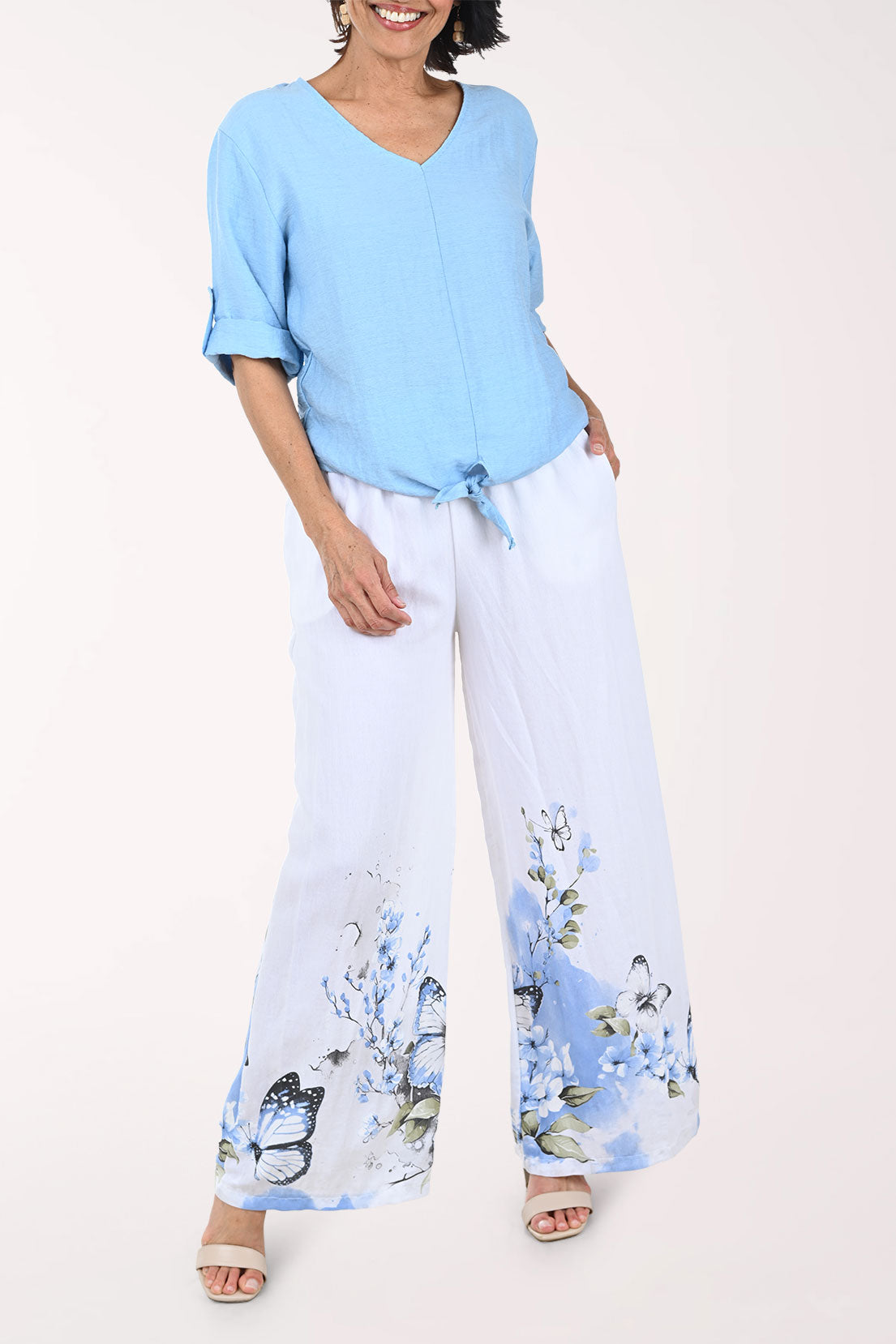Woman wearing a light blue top and white pants with floral patterns on a plain background
