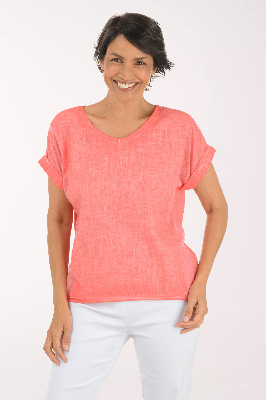 Woman wearing a coral pink top and white pants on a white background