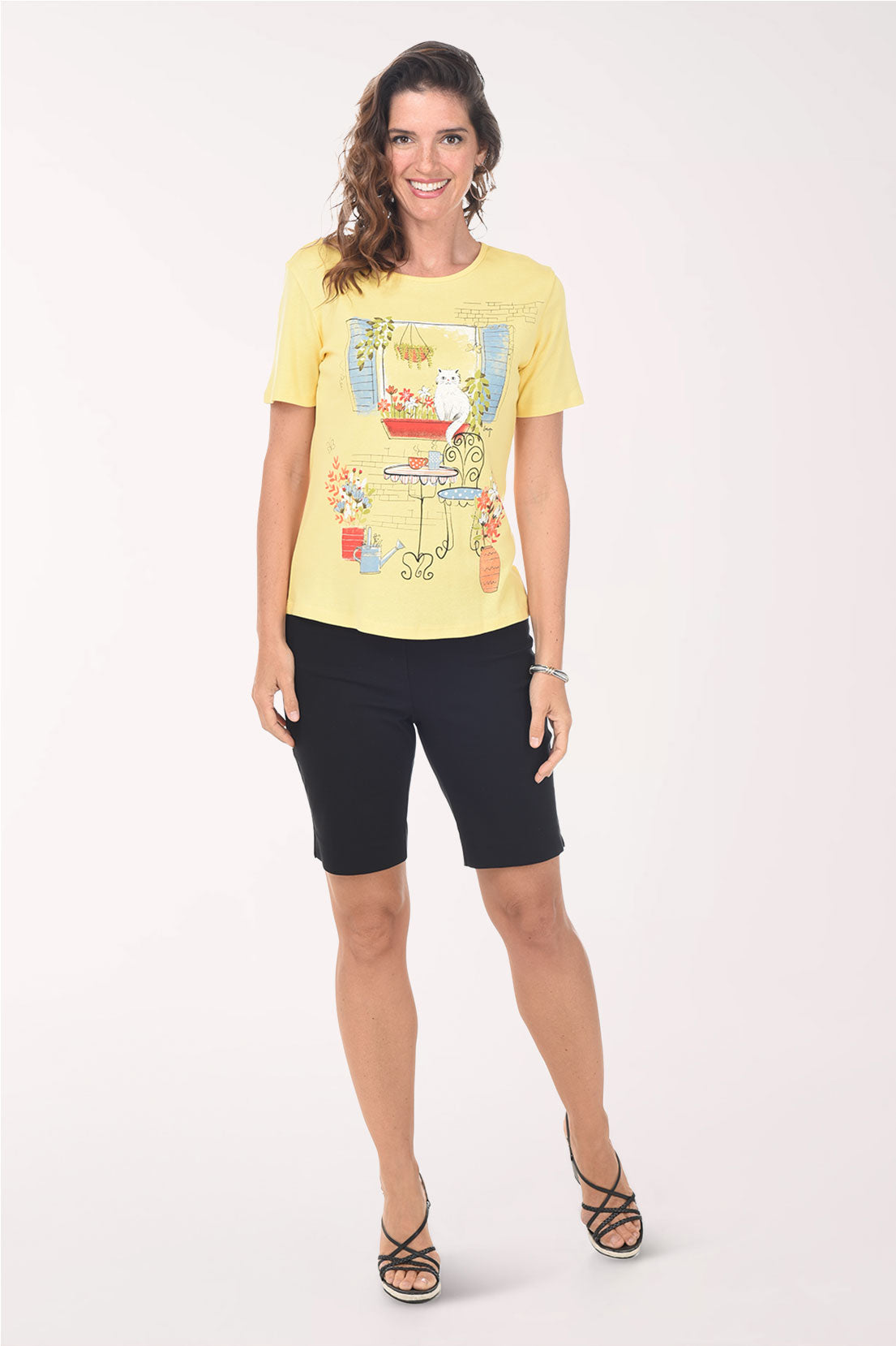 Woman wearing a yellow t-shirt with a graphic design and black shorts on a white background