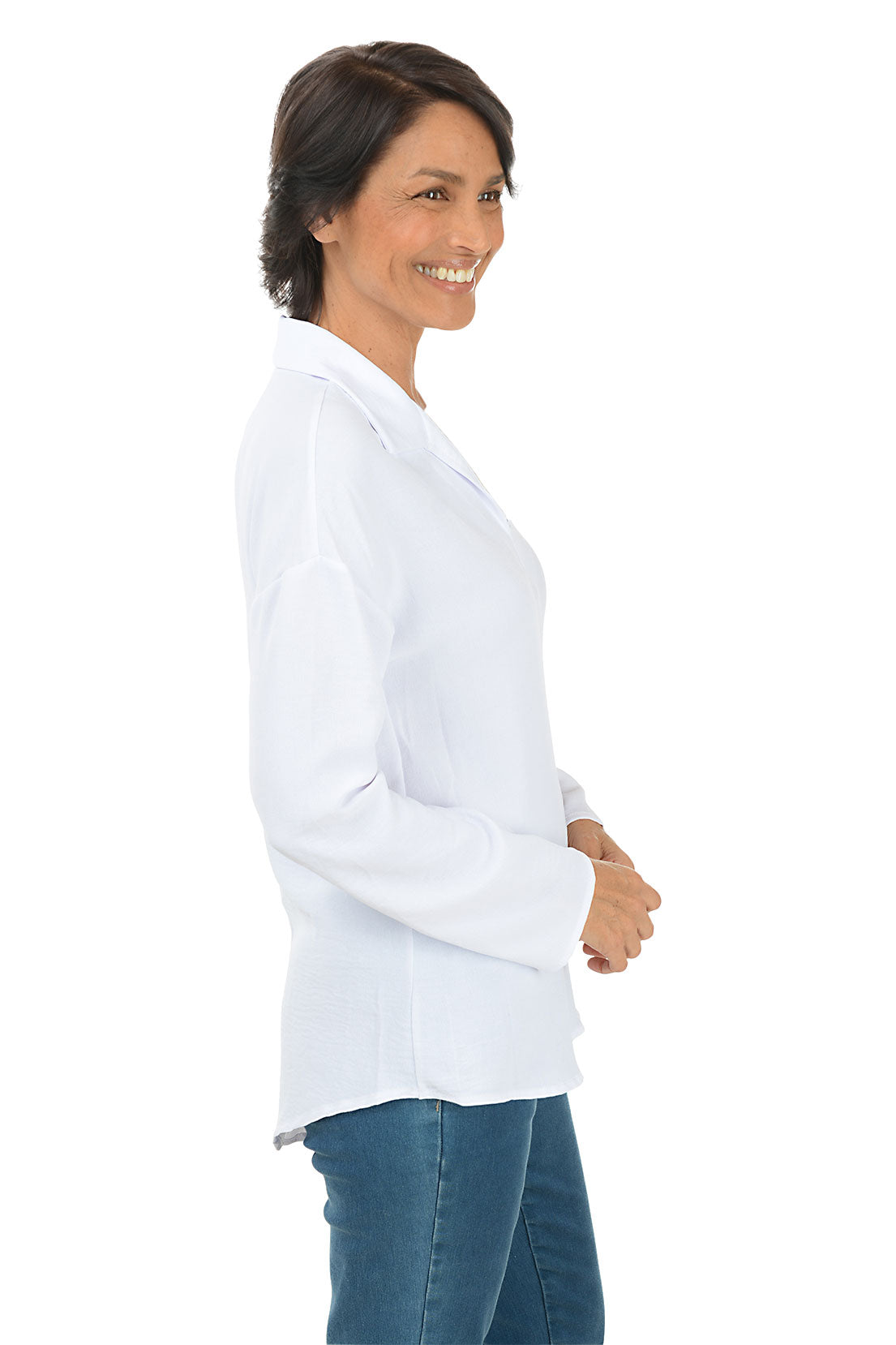 A side shot of a model wearing a white long sleeve blouse with a pointed foldover collar and button embellishment on the back. The blouse has a curved hemline and is made of crinkle fabric.