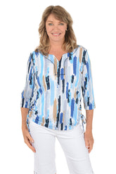 Woman wearing a blue and white patterned blouse with white pants on a white background.