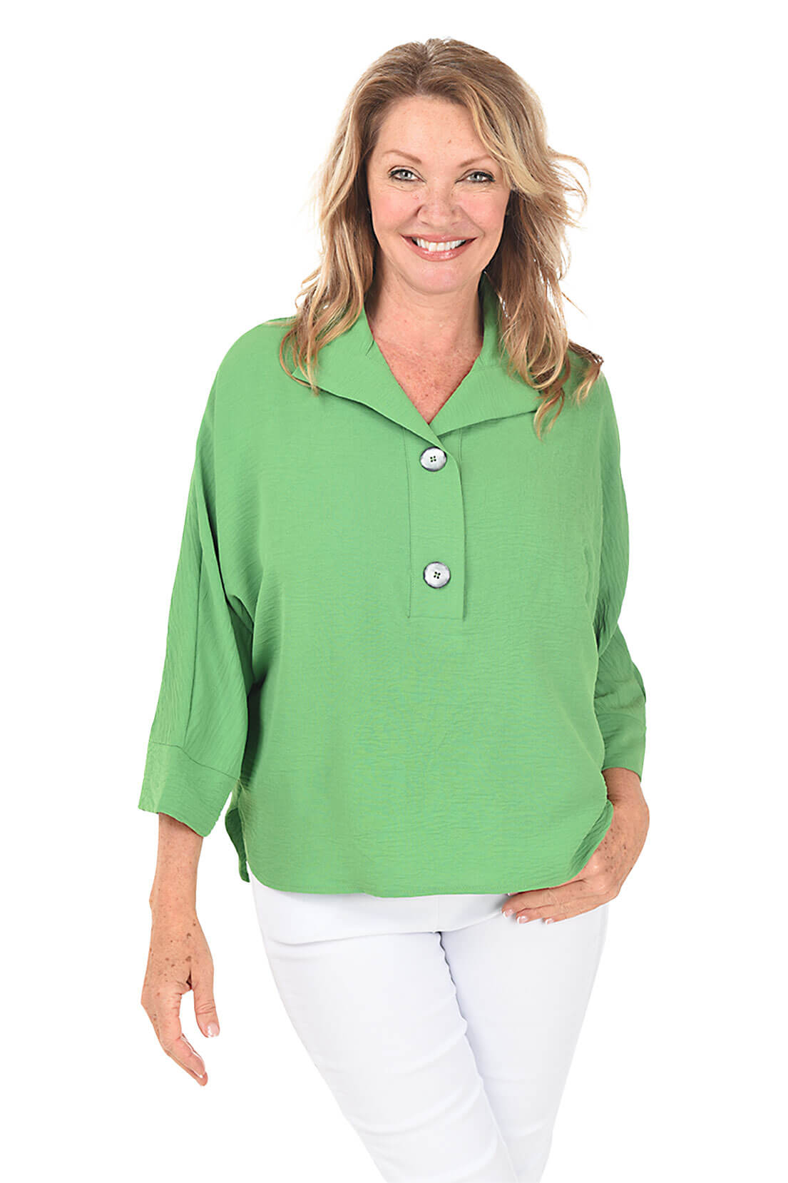 A front shot of a model wearing a green dolman sleeve blouse with a classic foldover collar and pearlescent button accents, paired with white pants.