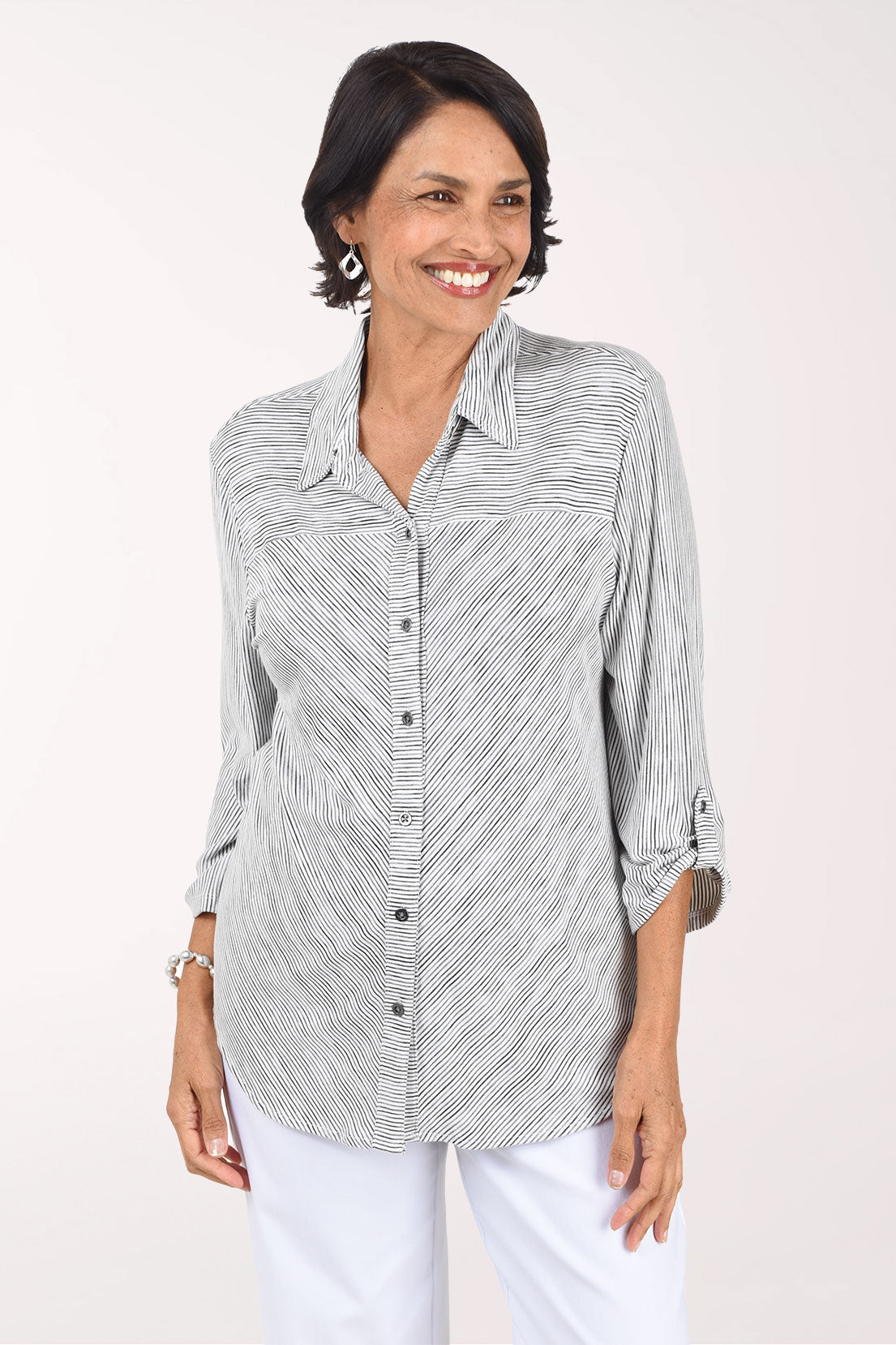 Front view of a woman in a white button-front knit shirt with fine wavy black stripes, a fold-over collar and rolled 3/4 sleeves with button tabs, worn with white pants.
