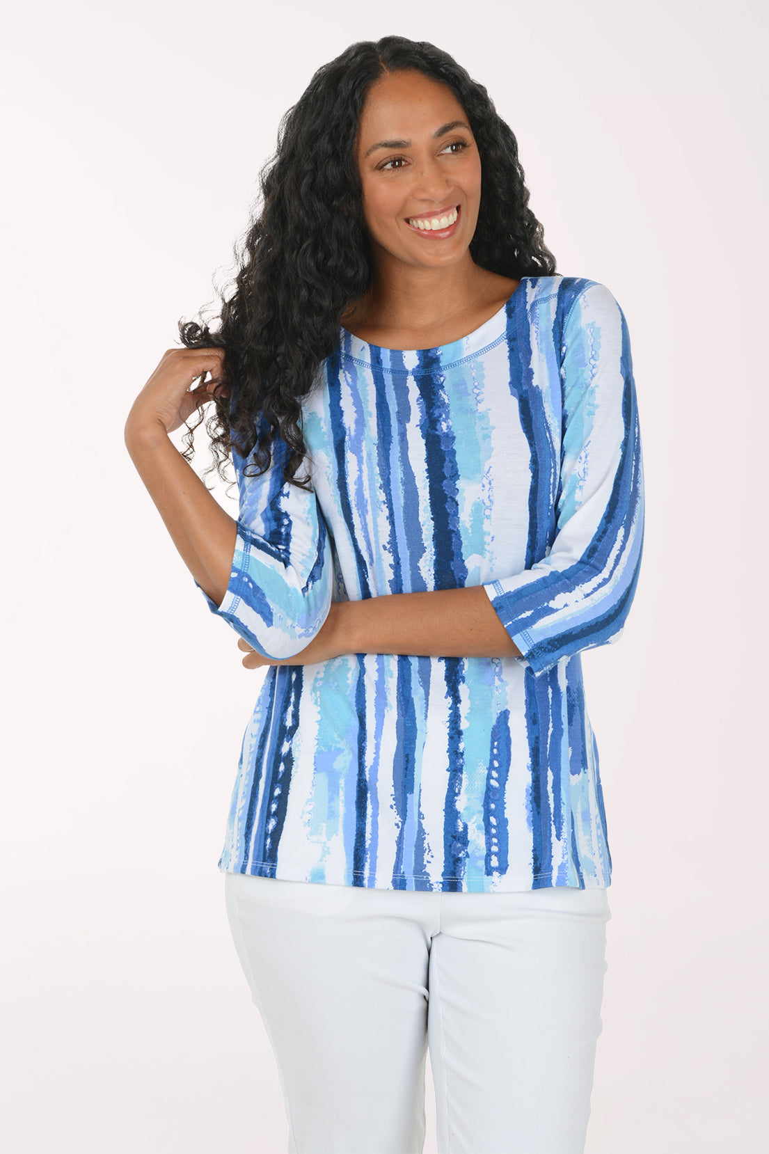 A woman modeling a blue and white vertically striped top with three-quarter sleeves, paired with white pants, against a plain white studio background.