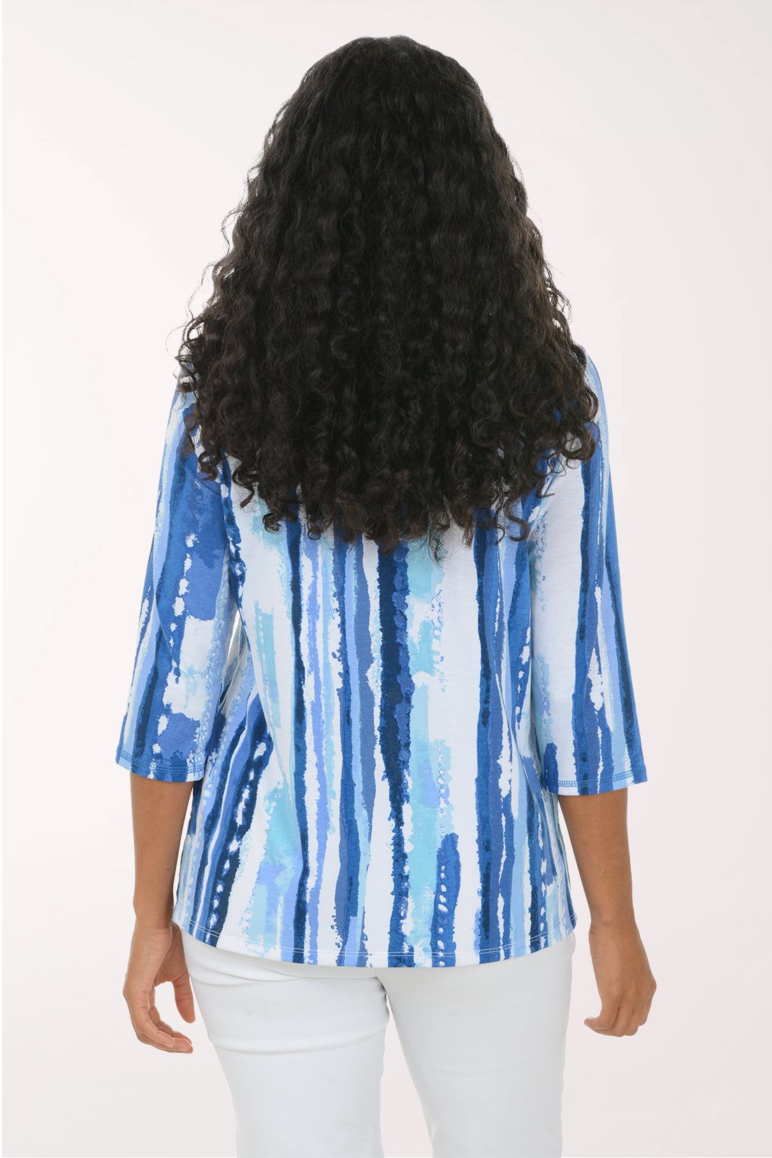 A woman modeling a blue and white vertically striped top with three-quarter sleeves, paired with white pants, against a plain white studio background.