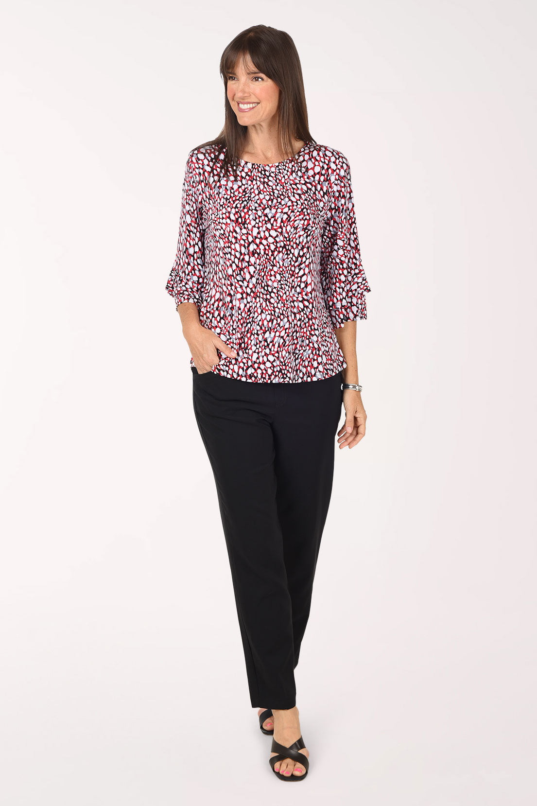 Full-length front view of a woman in black pull-on ankle pants with a slim straight leg, worn with the Spotted Ruffle Sleeve Top and black sandals.