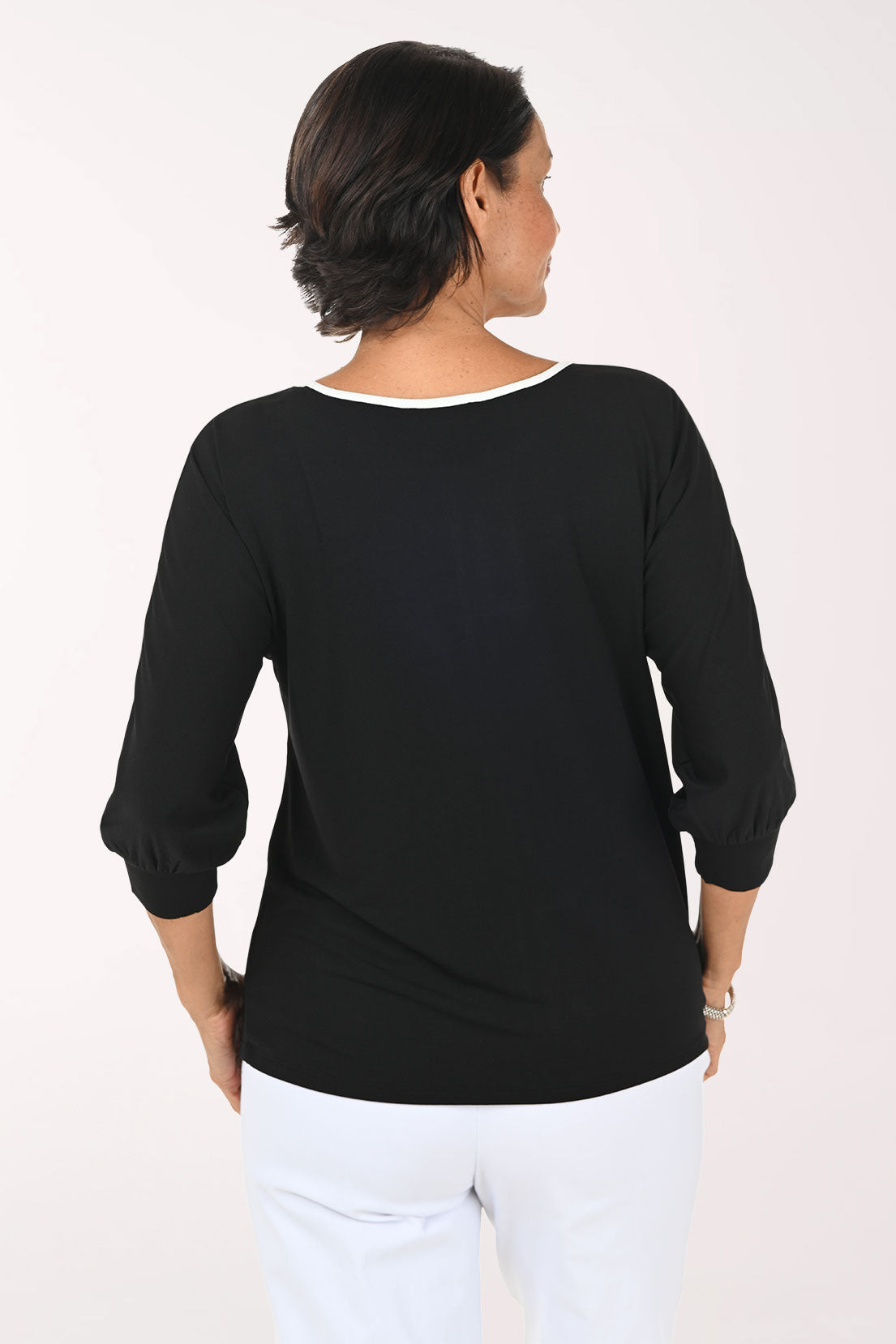 A woman shown from the back wearing a black three-quarter sleeve top with a white trim at the neckline, paired with white pants, against a plain white background.