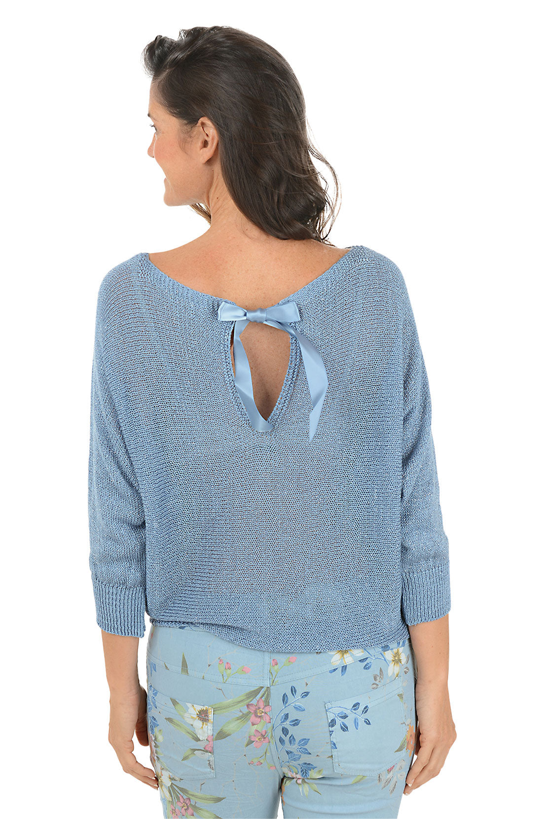Woman wearing a blue sweater with a bow detail on the back, standing against a white background.