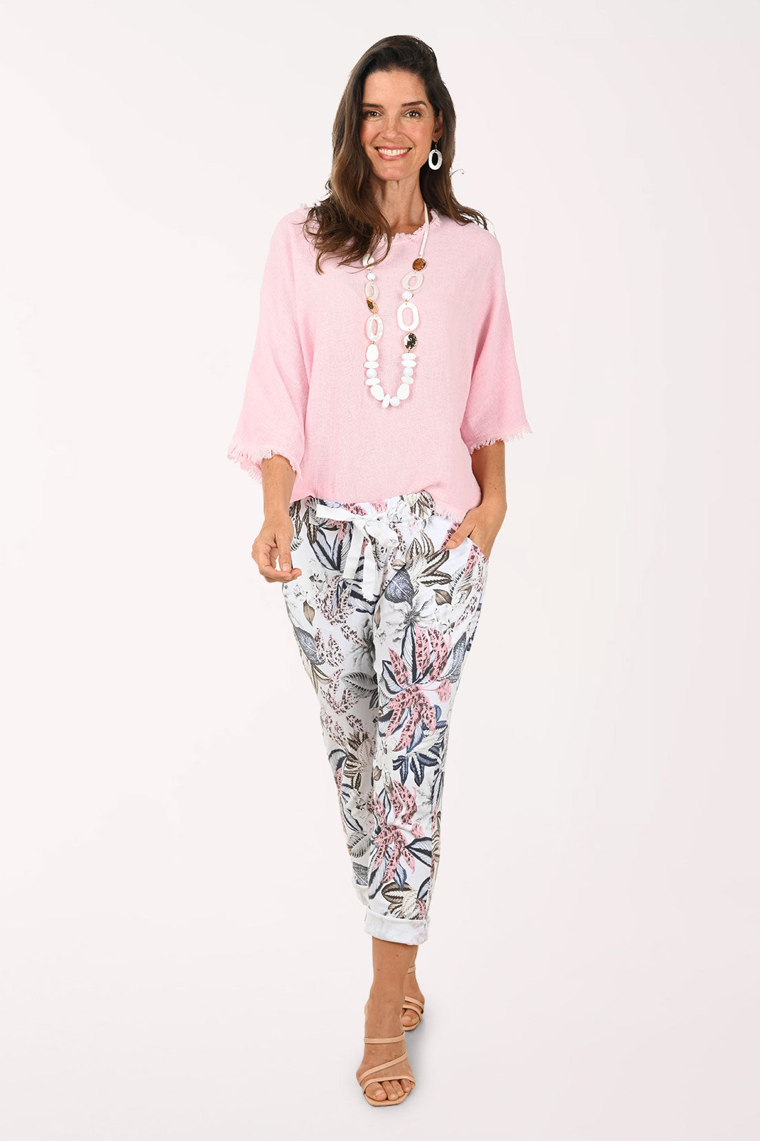 Woman wearing a light pink blouse with fringe details on a white background and multi patterned joggers