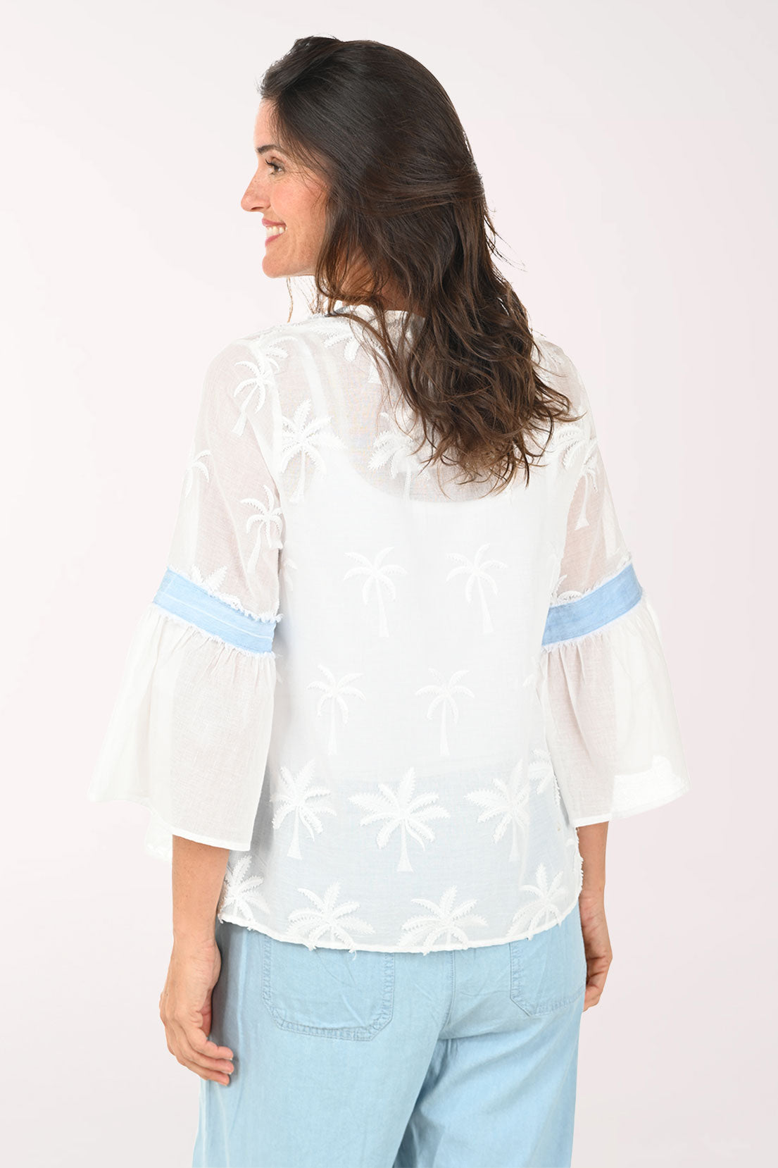 Woman wearing a white blouse with blue accents and light blue pants on a white background
