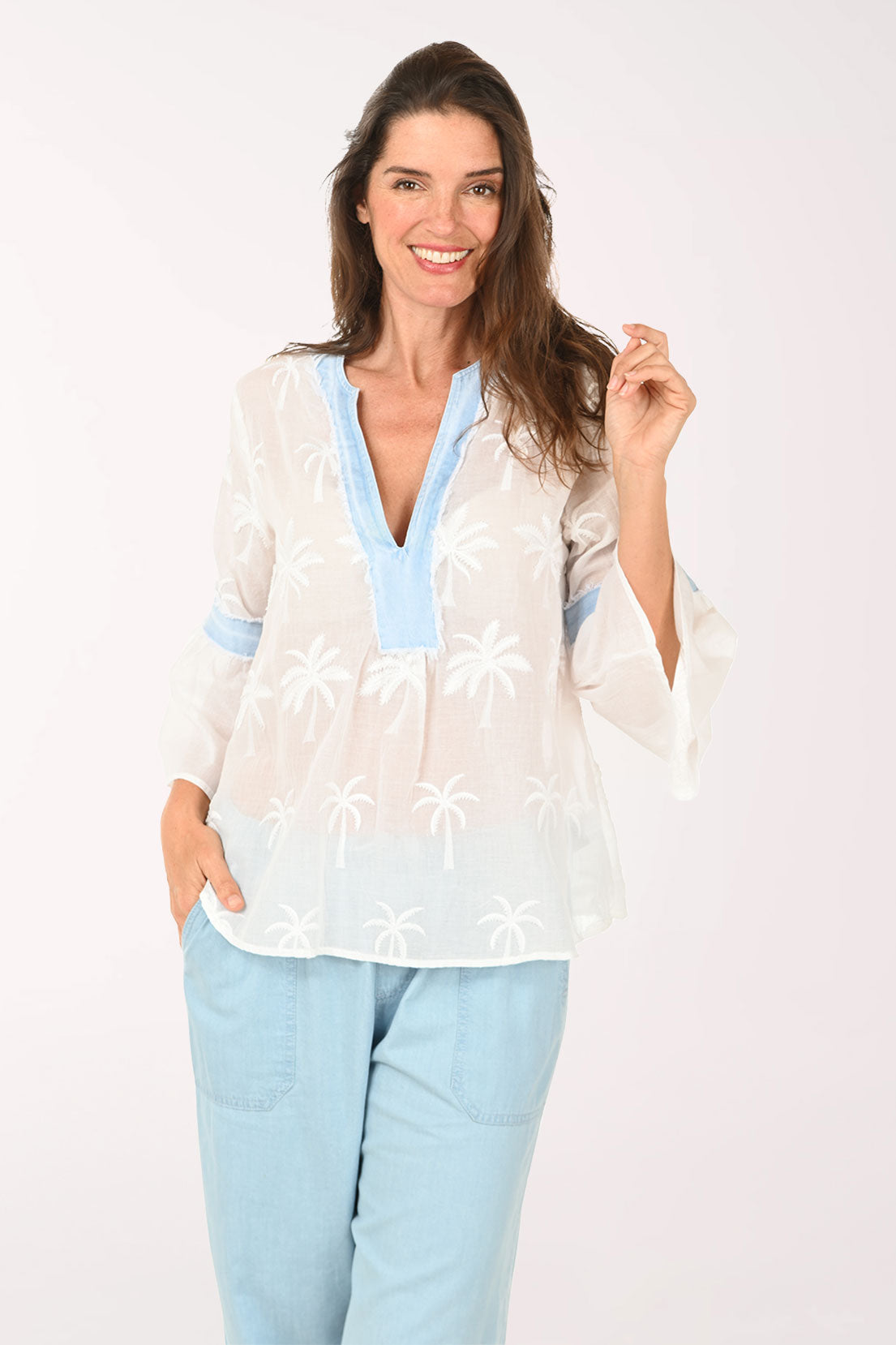 Woman wearing a white blouse with blue accents and light blue pants on a white background