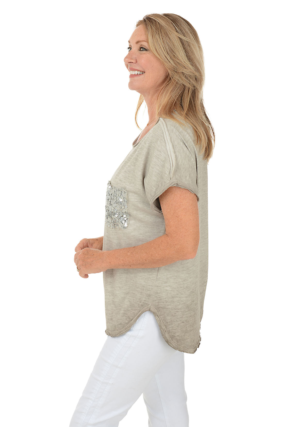A side shot of a model wearing a beige scoop neck tee with short dolman sleeves and a sequined left chest pocket, paired with white pants.