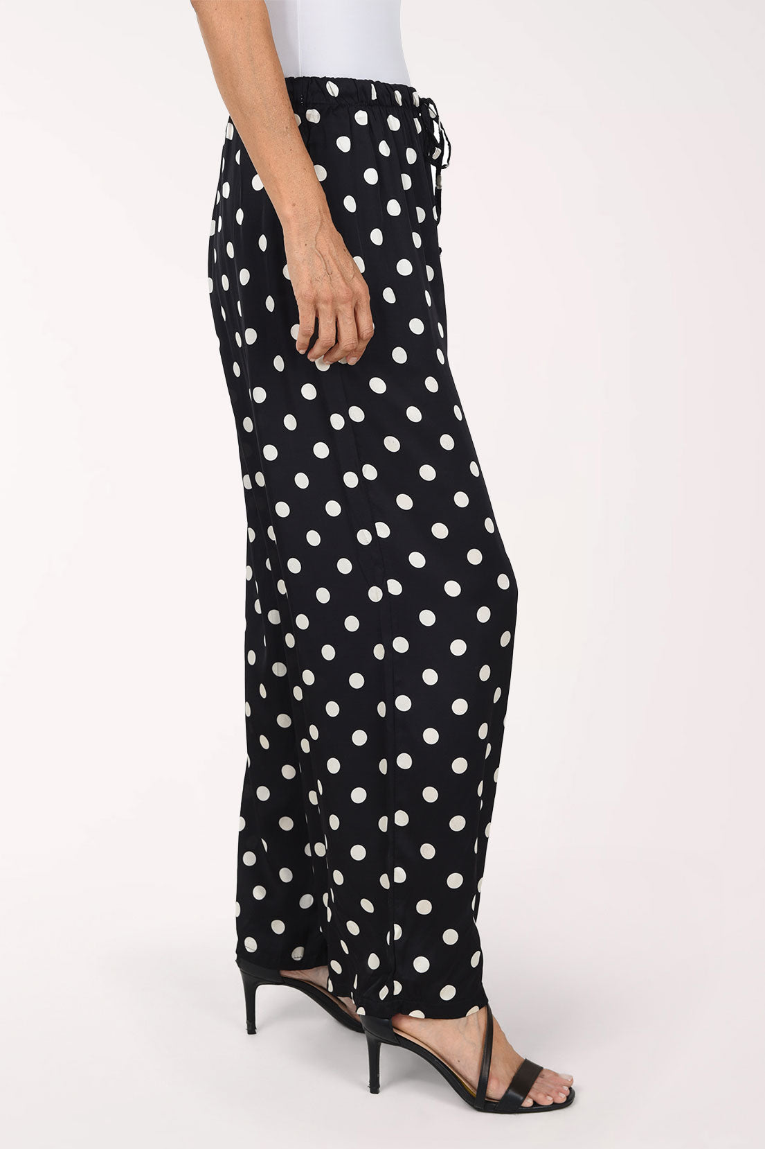 Black wide-leg pants with a white polka dot pattern, shown on a model wearing black strappy heels against a plain white studio background.