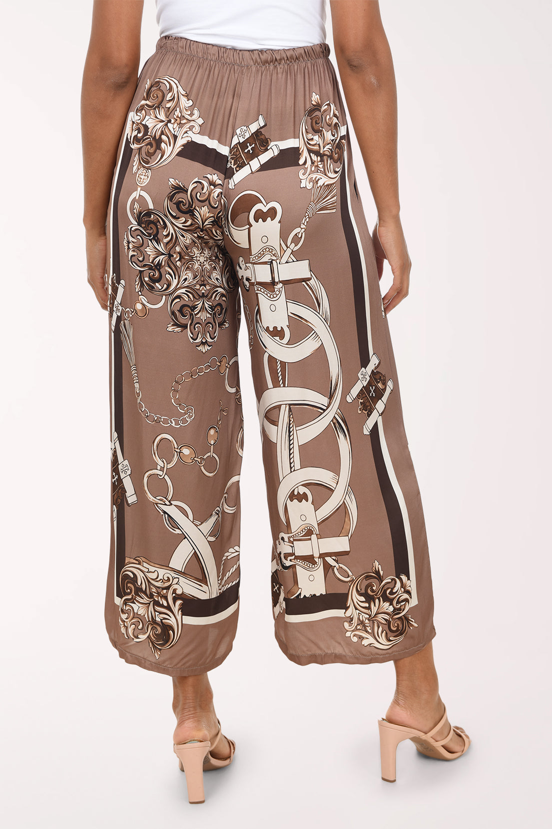 A person wearing wide-leg cropped pants with an ornate chain and floral print in taupe, beige, and brown, shown from the back against a plain light background.