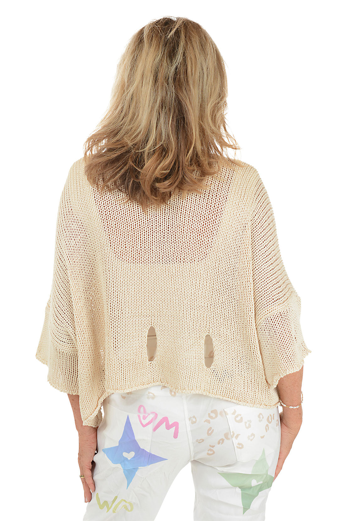 A back shot of a model wearing a beige open knit slouchy sweater with a scoop neck and 3/4-length dolman sleeves. The sweater has a shark bite hemline with cut-out details.