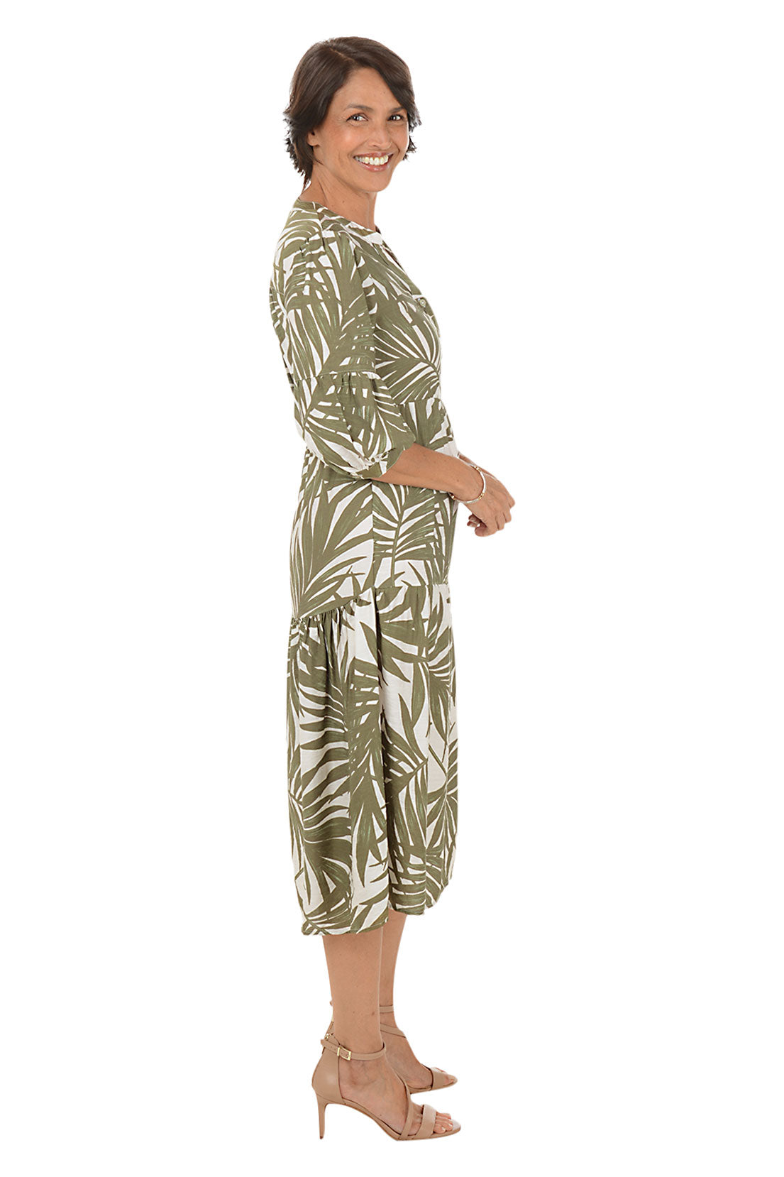 Woman wearing a green and white leaf-patterned dress on a white background. Side shot.