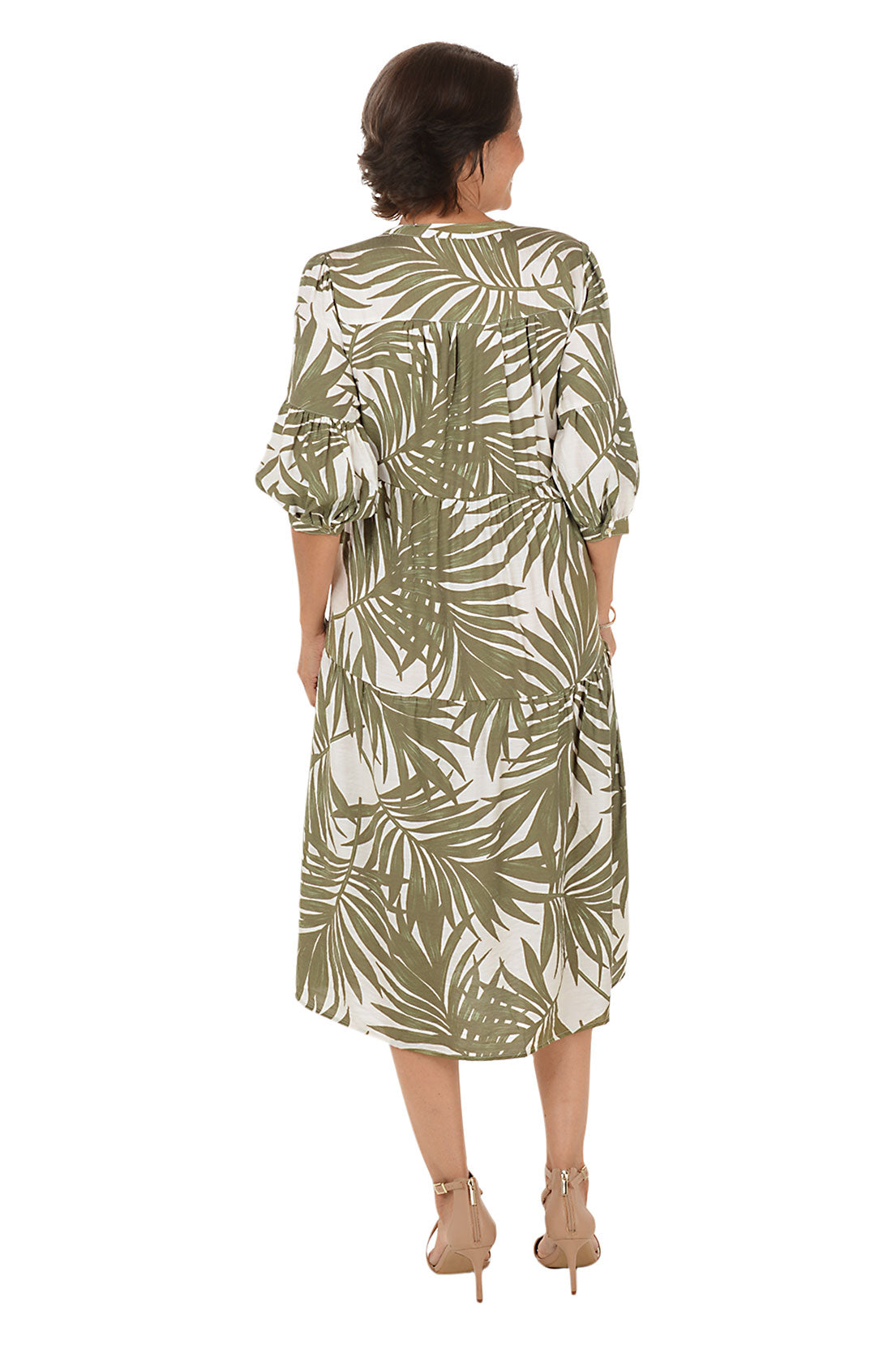 Woman wearing a green and white leaf-patterned dress on a white background. Back shot.