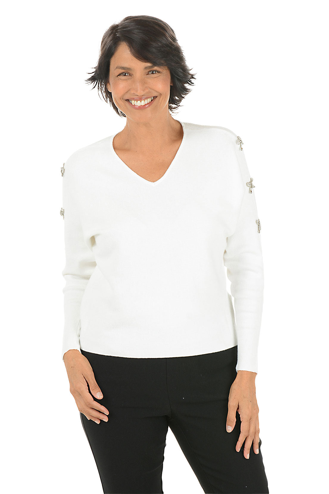 Woman wearing a white sweater with rhinestone bow embellishments on the sleeves on a white background.