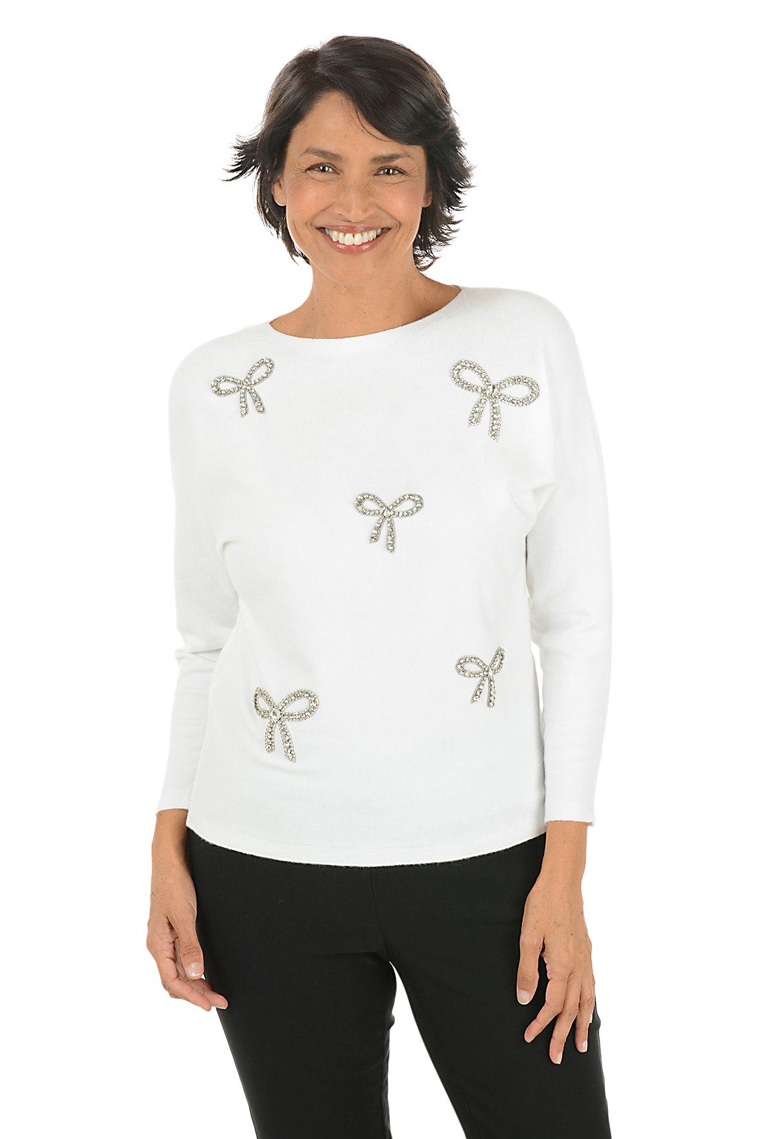 Woman wearing a white long sleeve sweater with rhinestone bow embellishments.