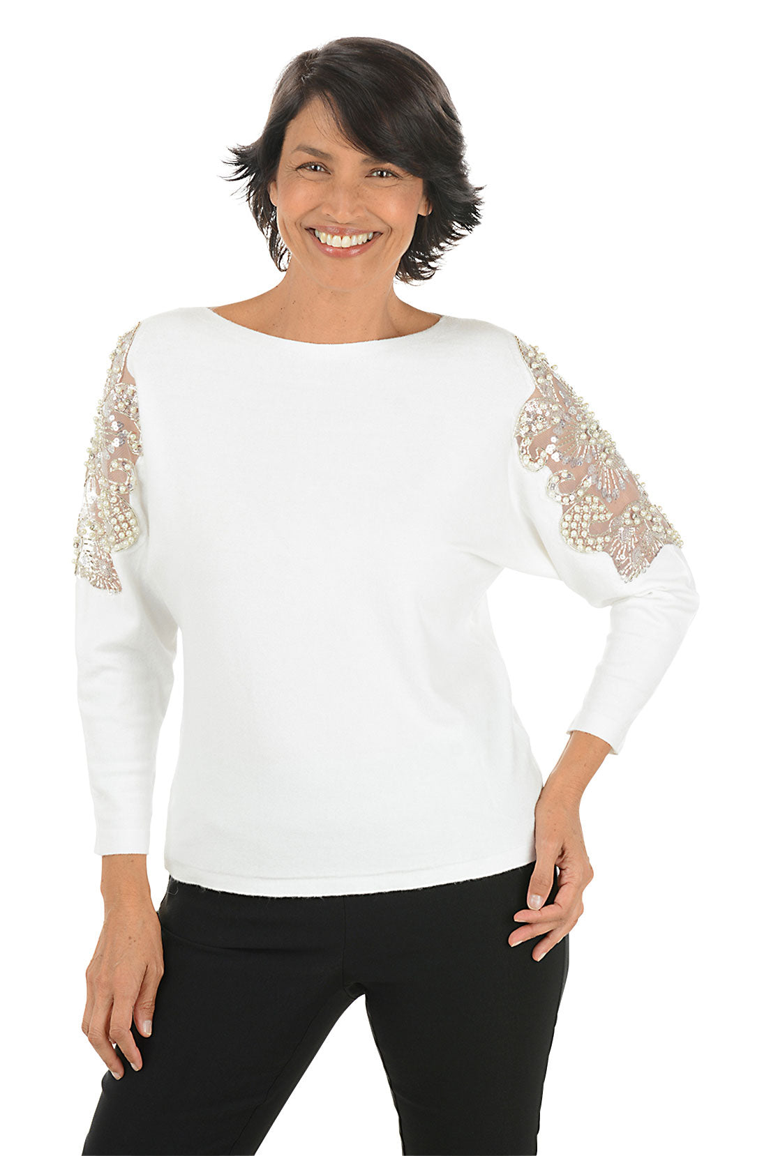 Woman wearing a long sleeve white sweater with floral embellished appliques on the arm.