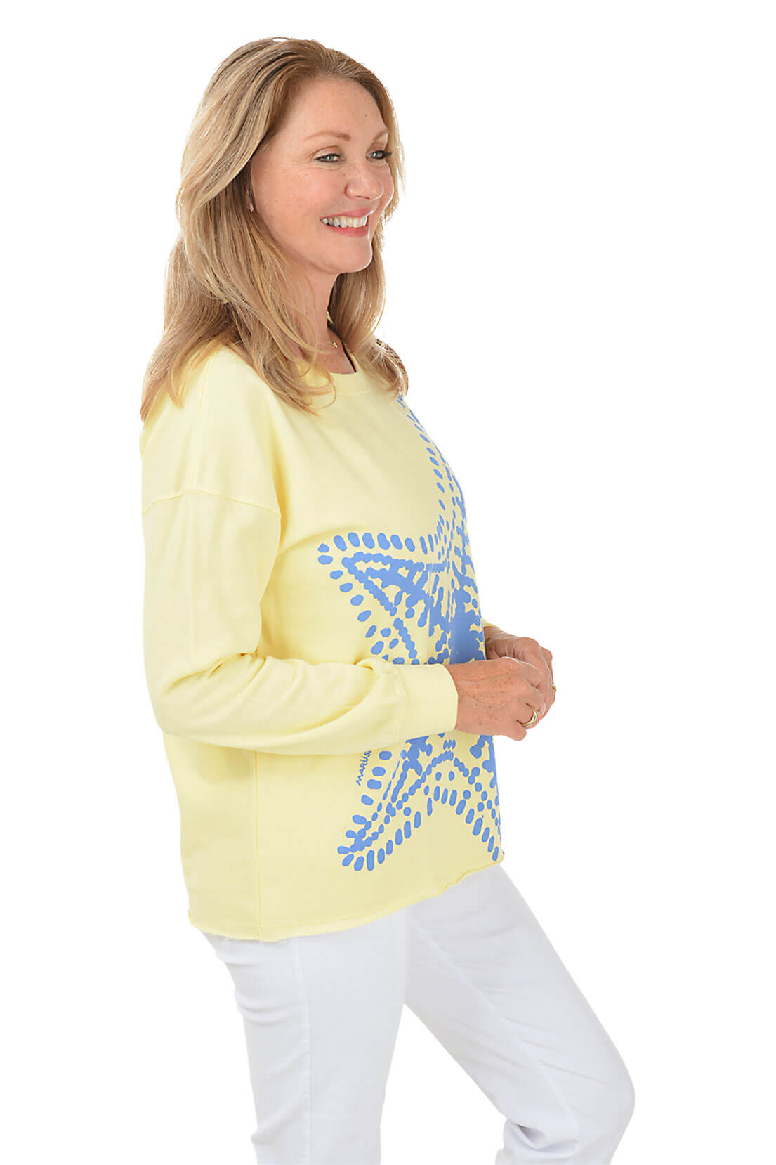 Side shot of a woman wearing a light yellow long-sleeve top with a blue star design on a white background