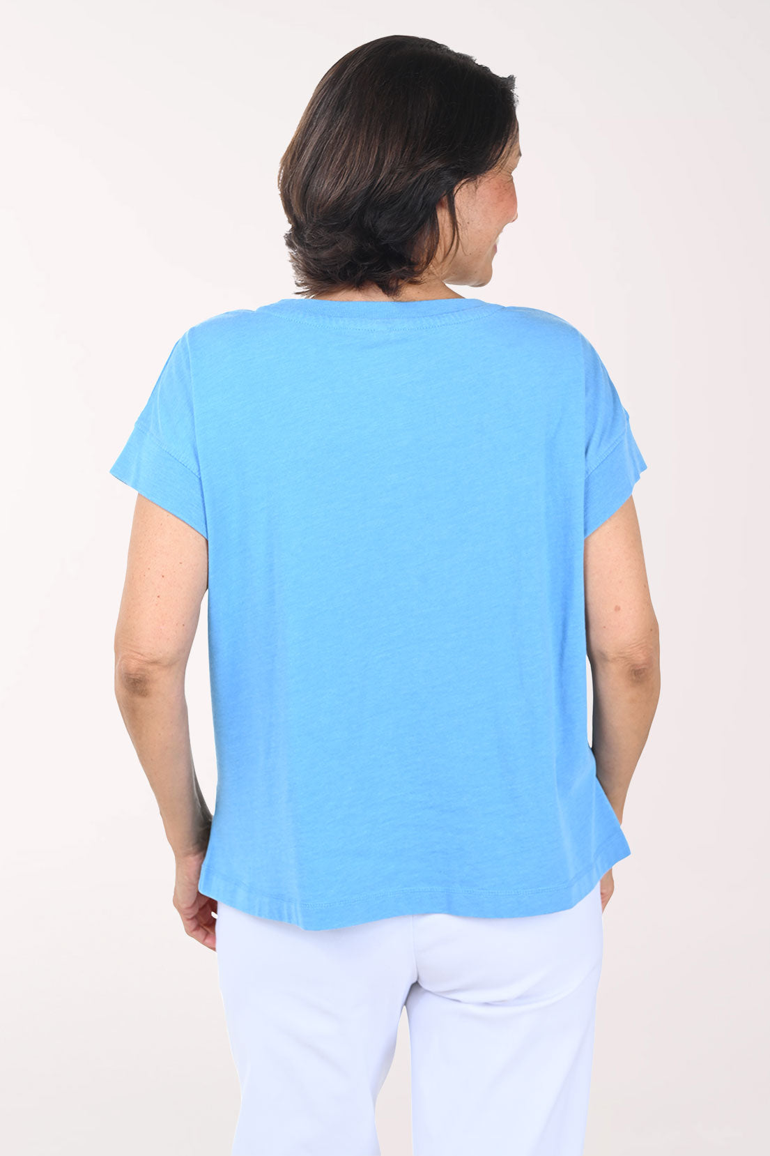 Woman wearing a light blue t-shirt with a white graphic design on a plain background