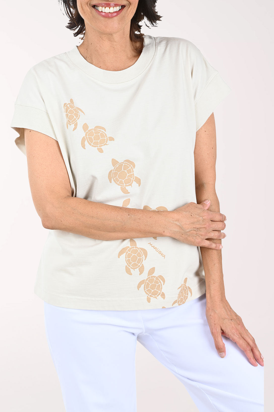 Woman wearing a beige t-shirt with turtle patterns on a plain background
