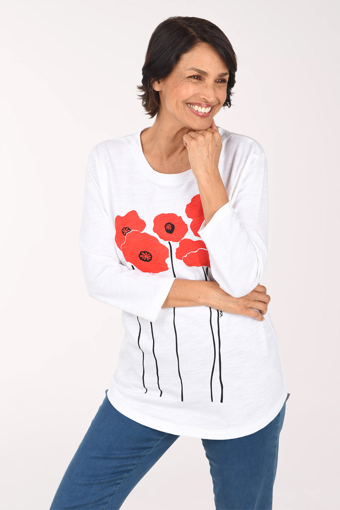 Woman with her hand at her chin wearing the white poppy tunic, showing the 3/4-length sleeves and curved hem over jeans