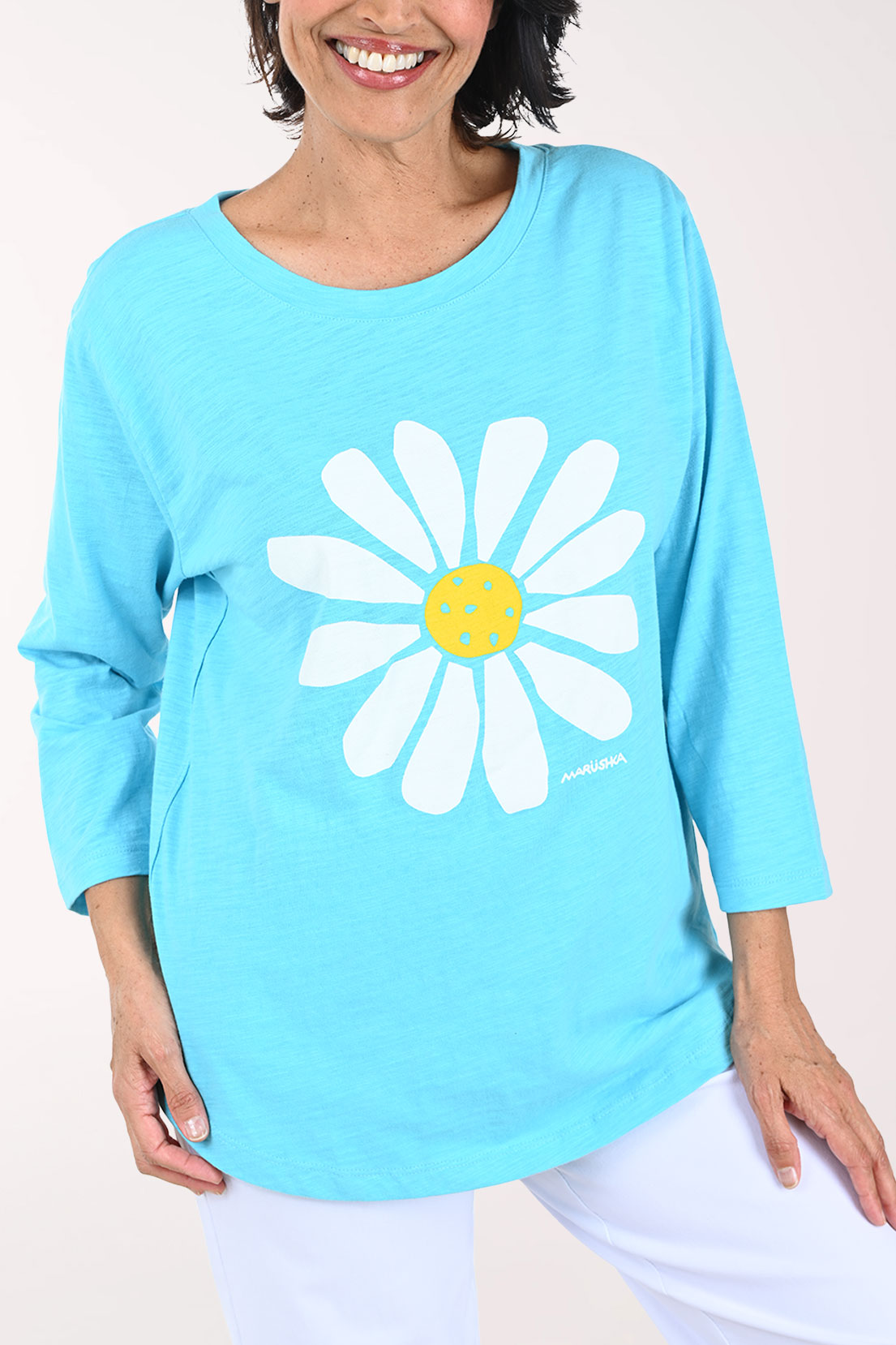 Woman wearing a light blue tunic top with a white daisy design on a plain background