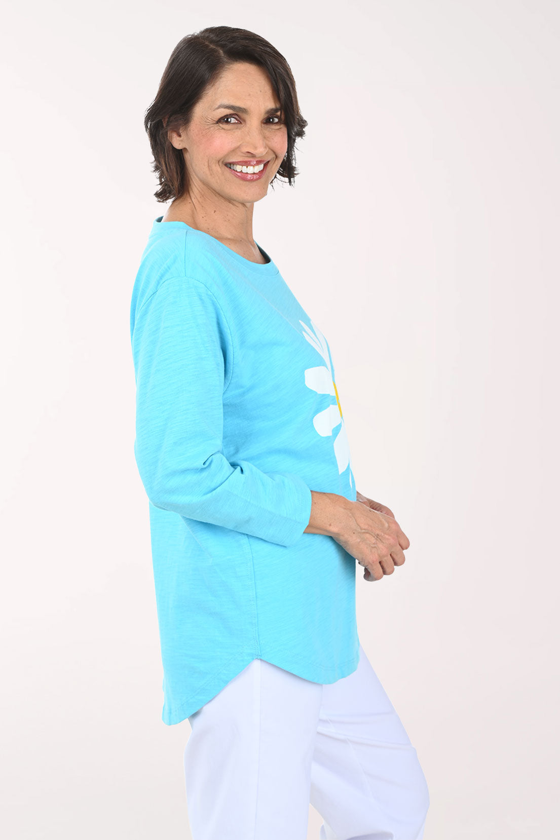 Woman wearing a light blue tunic top with a white daisy design on a plain background