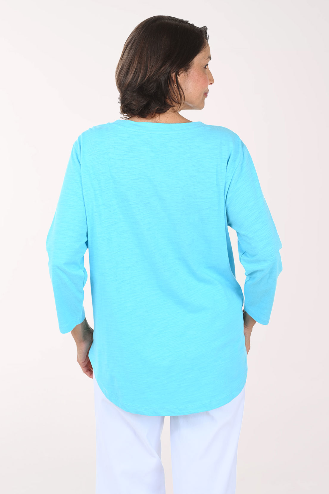 Woman wearing a light blue tunic top with a white daisy design on a plain background