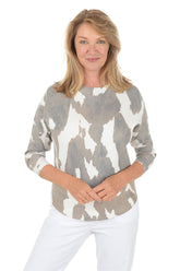 Woman wearing a gray and white cow patterned sweater with white pants on a white background.