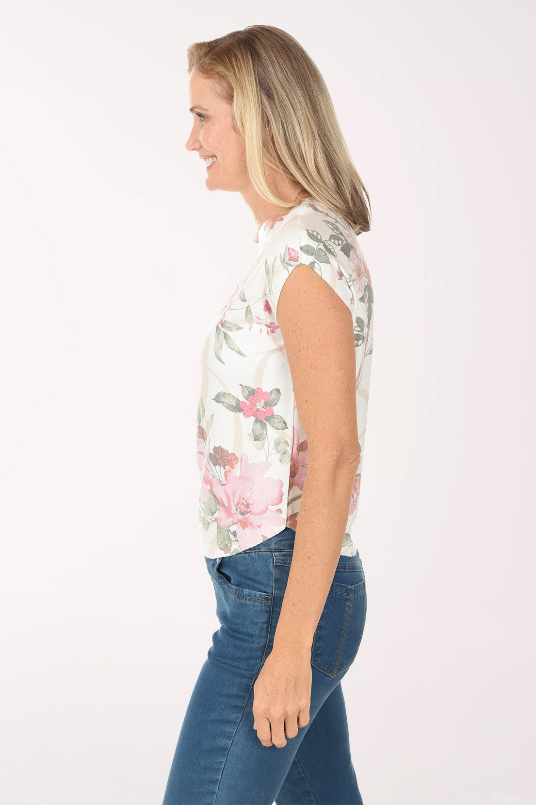 Woman wearing a sleeveless floral top and blue jeans on a white background