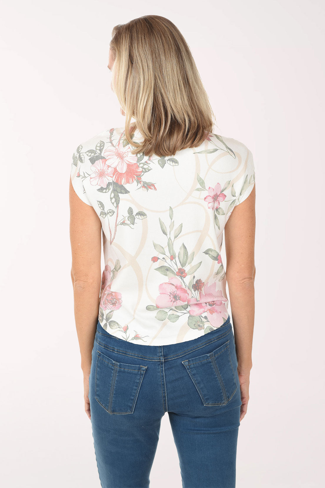 Woman wearing a sleeveless floral top and blue jeans on a white background