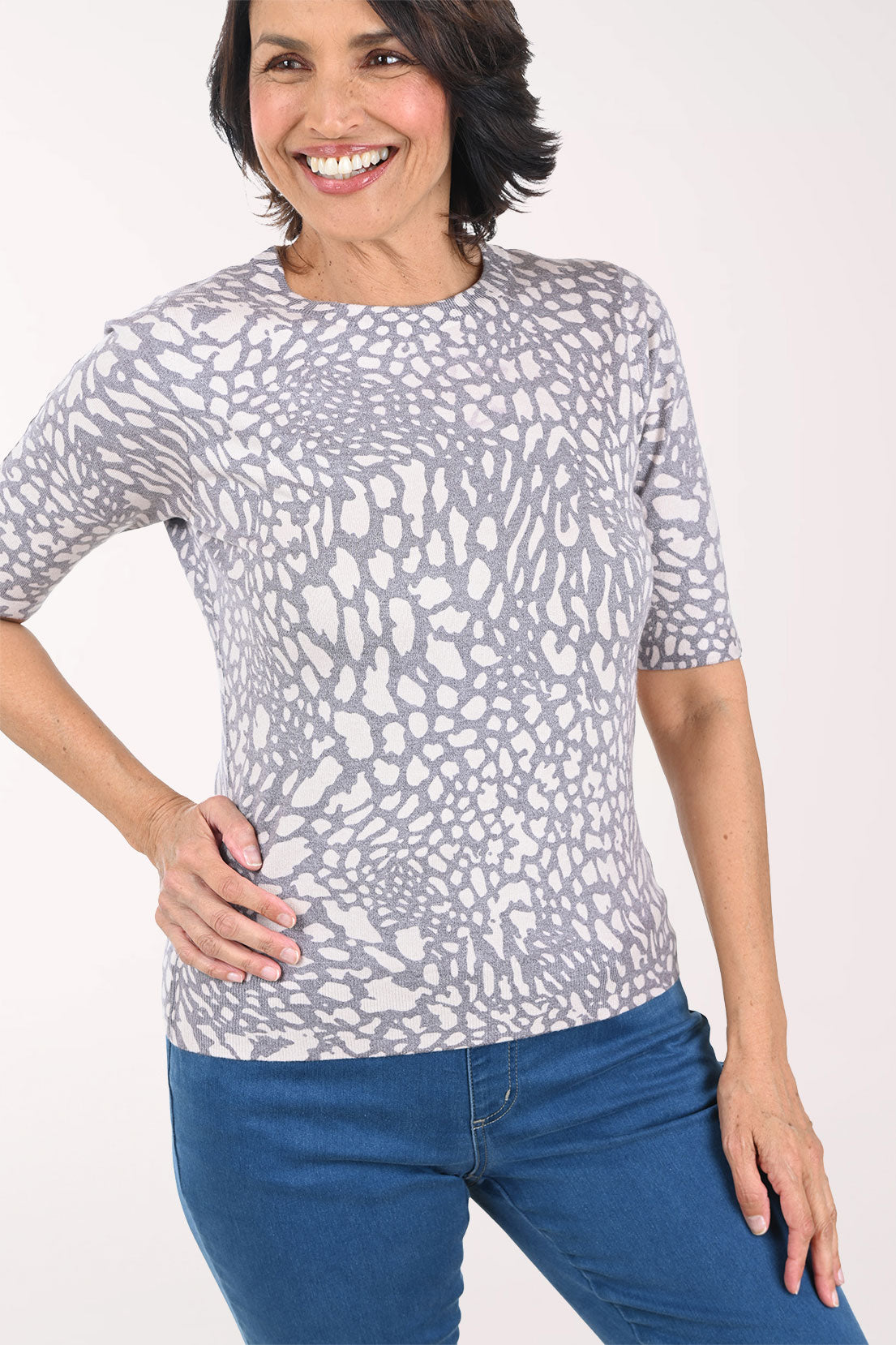 Woman wearing a patterned gray sweater and blue jeans on a white background