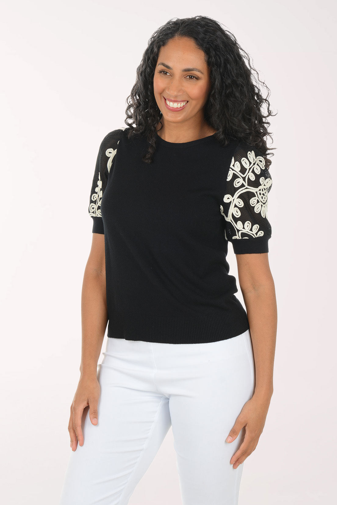 Woman wearing a black top with floral embellishments on sleeves against a white background