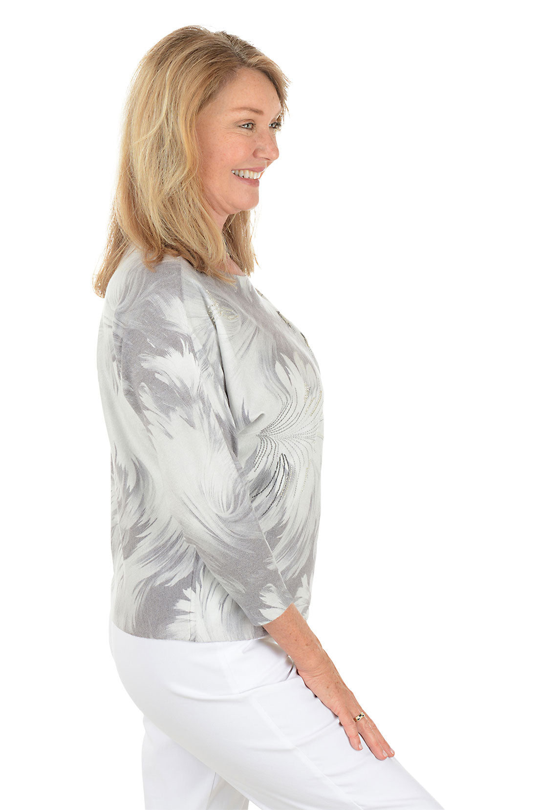 Woman wearing a 3/4 sleeve gray dandelion floral sweater with white pants on a white background. Side shot.